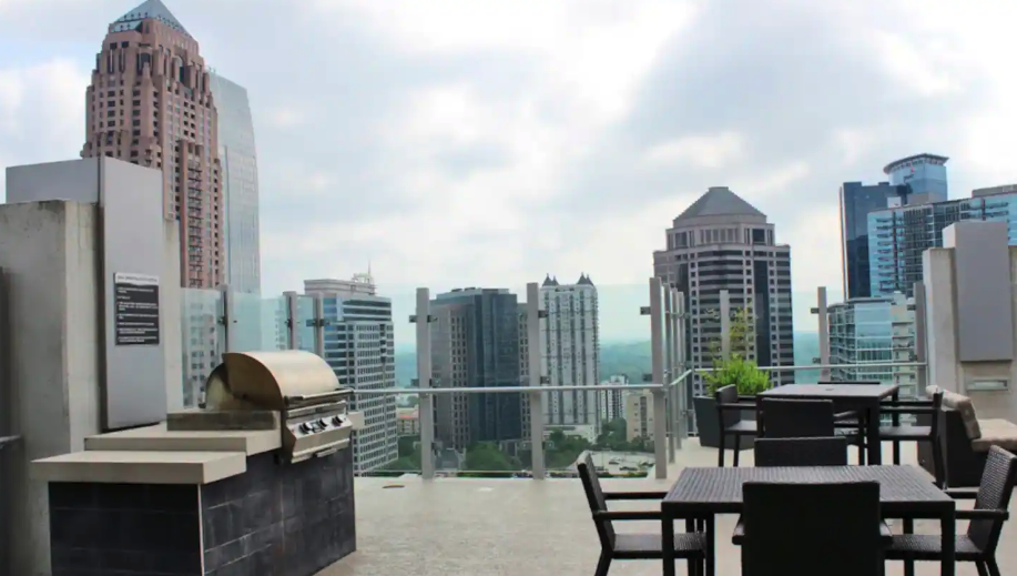 Rooftop terrace with grill and outdoor dining tables overlooking a city skyline with skyscrapers.