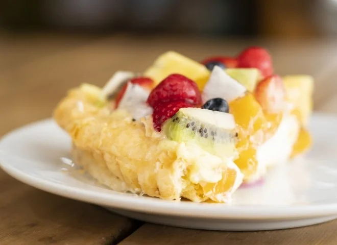 A slice of fruit tart with various fresh fruit toppings on a white plate.