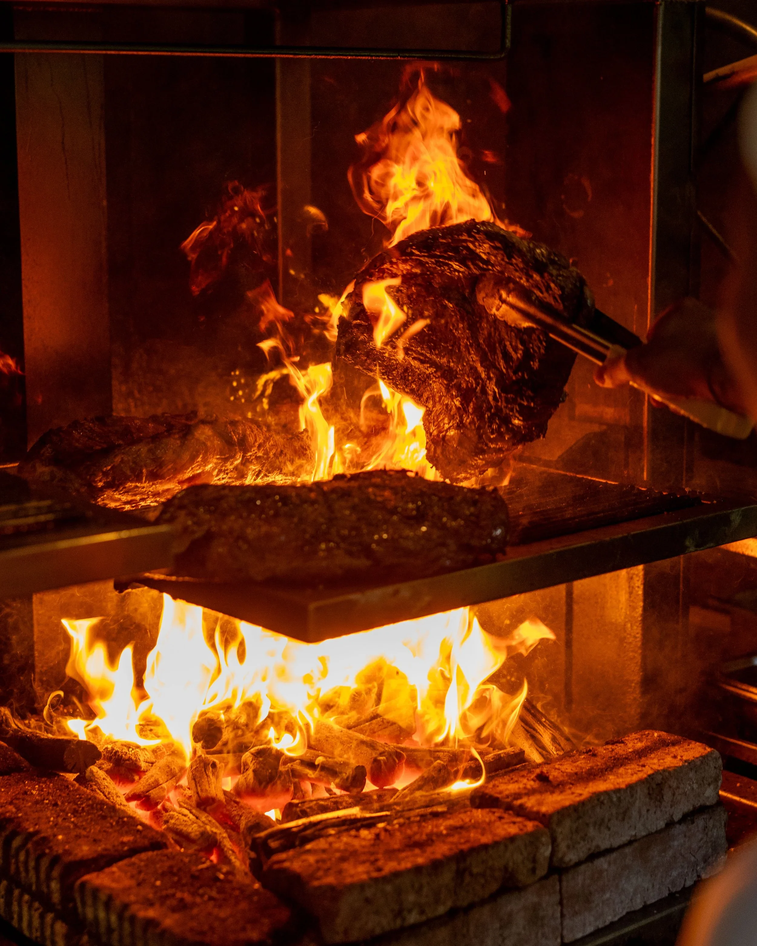 Burning logs and rocks inside an indoor fireplace with flames and glowing embers.