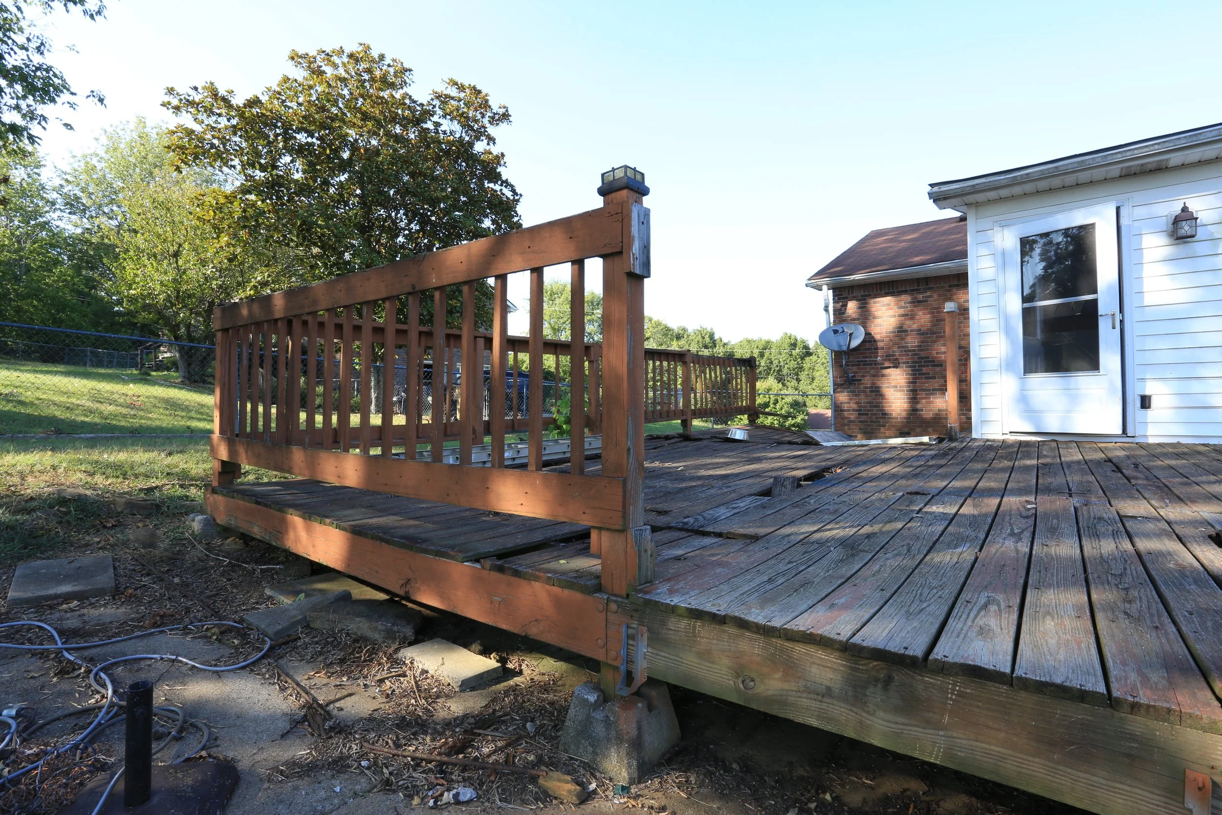 Backyard wooden deck attached to a house, with a railing and some construction work ongoing, as some floorboards are missing.