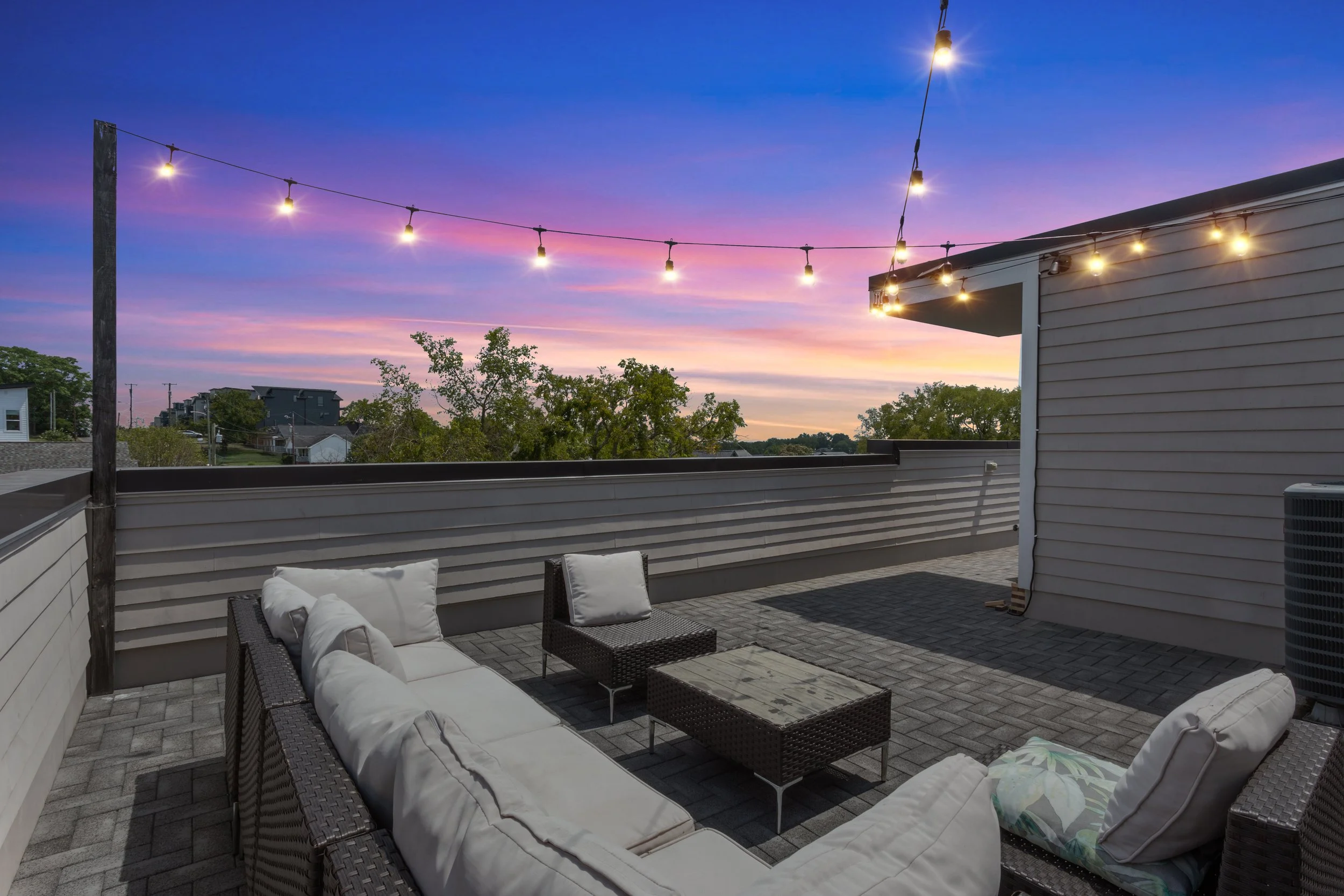 Outdoor rooftop patio with wicker furniture and string lights at sunset.