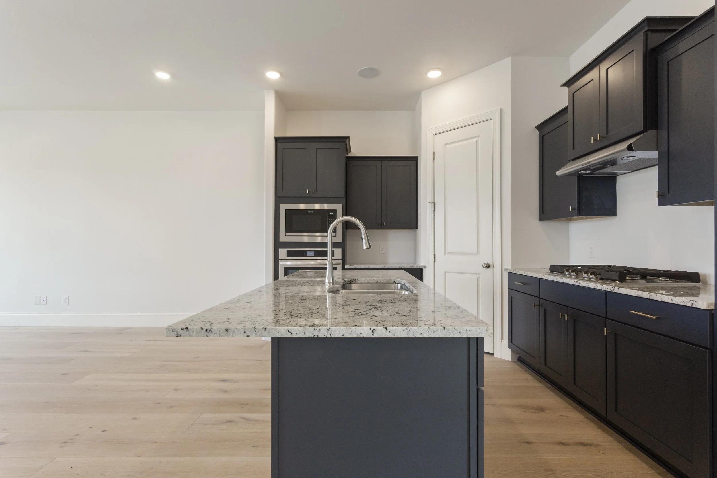 Modern kitchen with dark blue cabinets, marble countertops, an island with a sink, and a white door at the back wall.