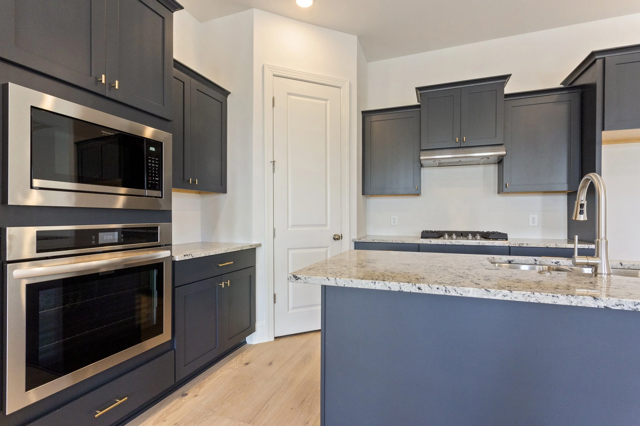 Modern kitchen with dark gray cabinets, granite countertops, stainless steel appliances including a microwave and oven, and a island with a sink.