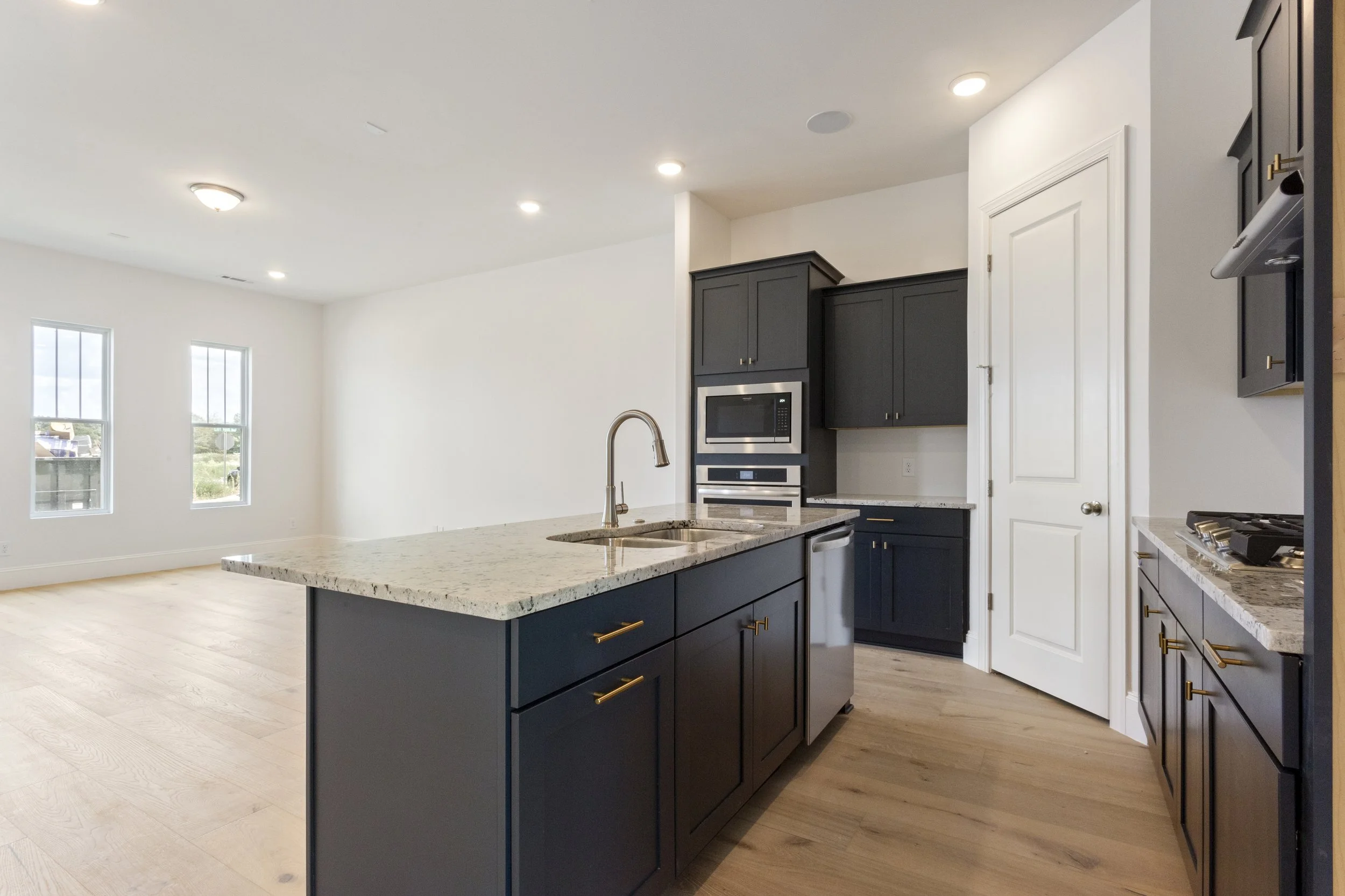 Modern kitchen with dark cabinets, granite countertops, stainless steel appliances, and light hardwood floors.