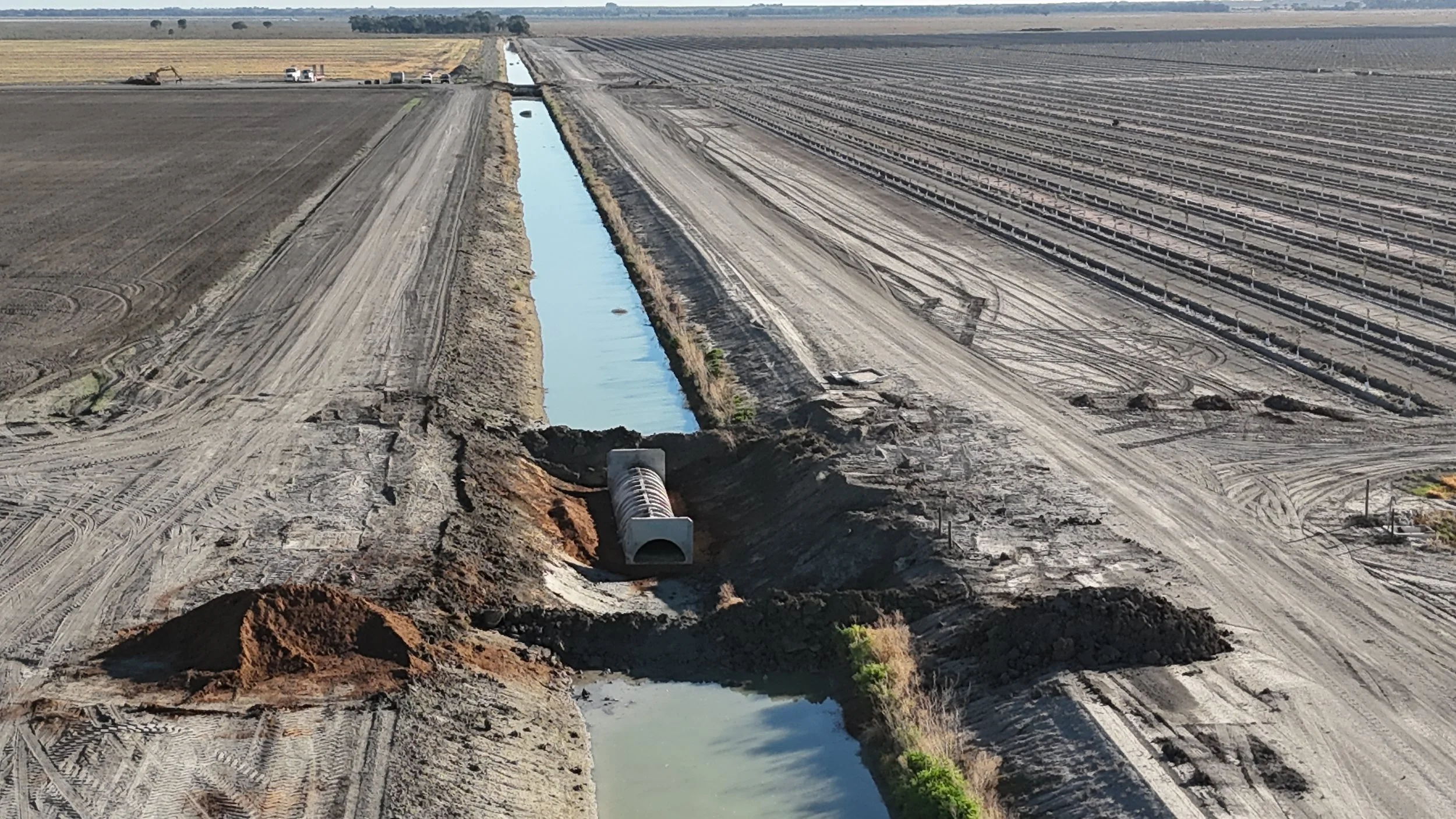 Construction site with trenches and a pipe, erosion control, and machinery on a farmland landscape.