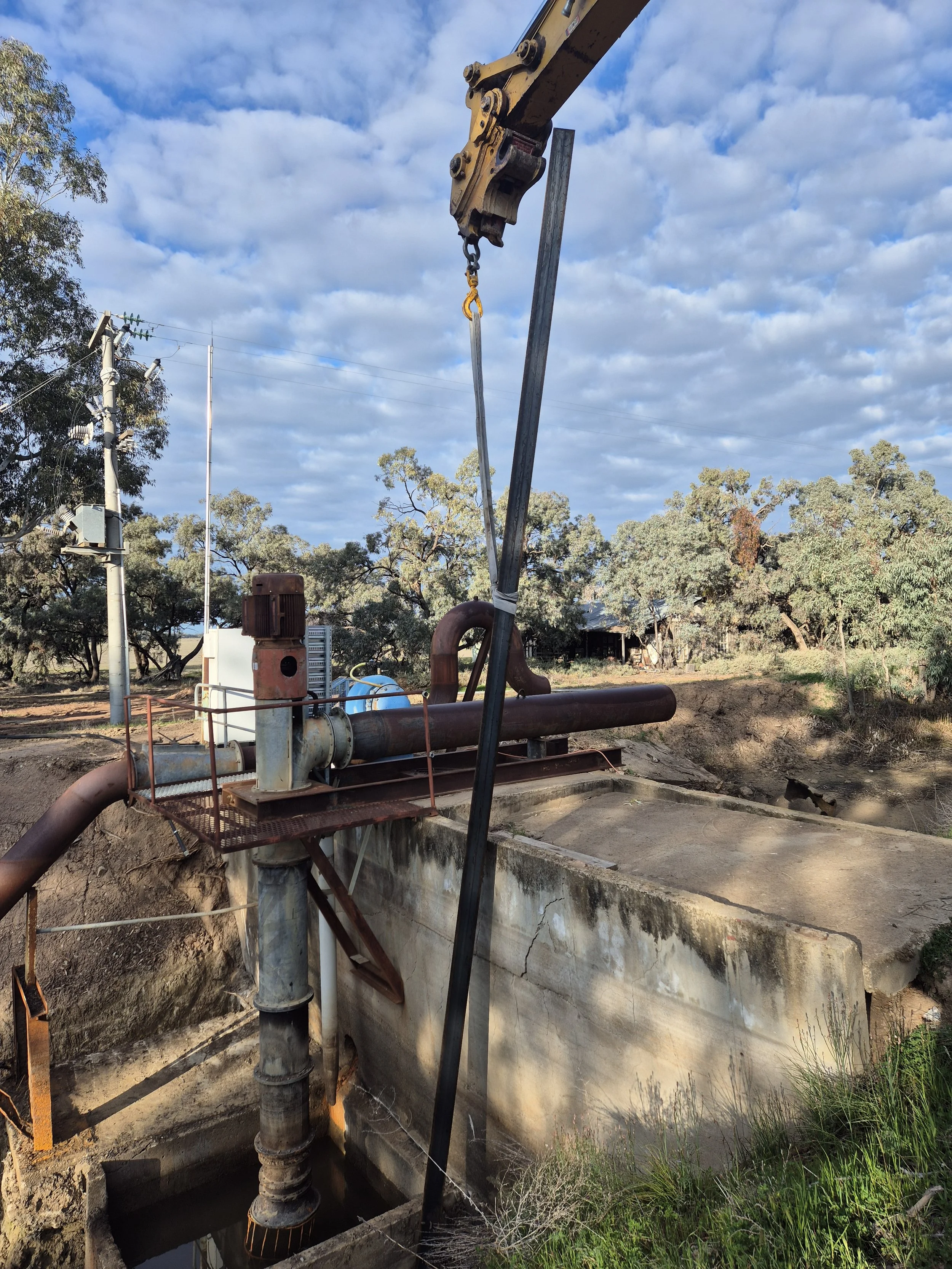 Outdoor scene with a large pipe and industrial machinery, trees and a partly cloudy sky in the background.