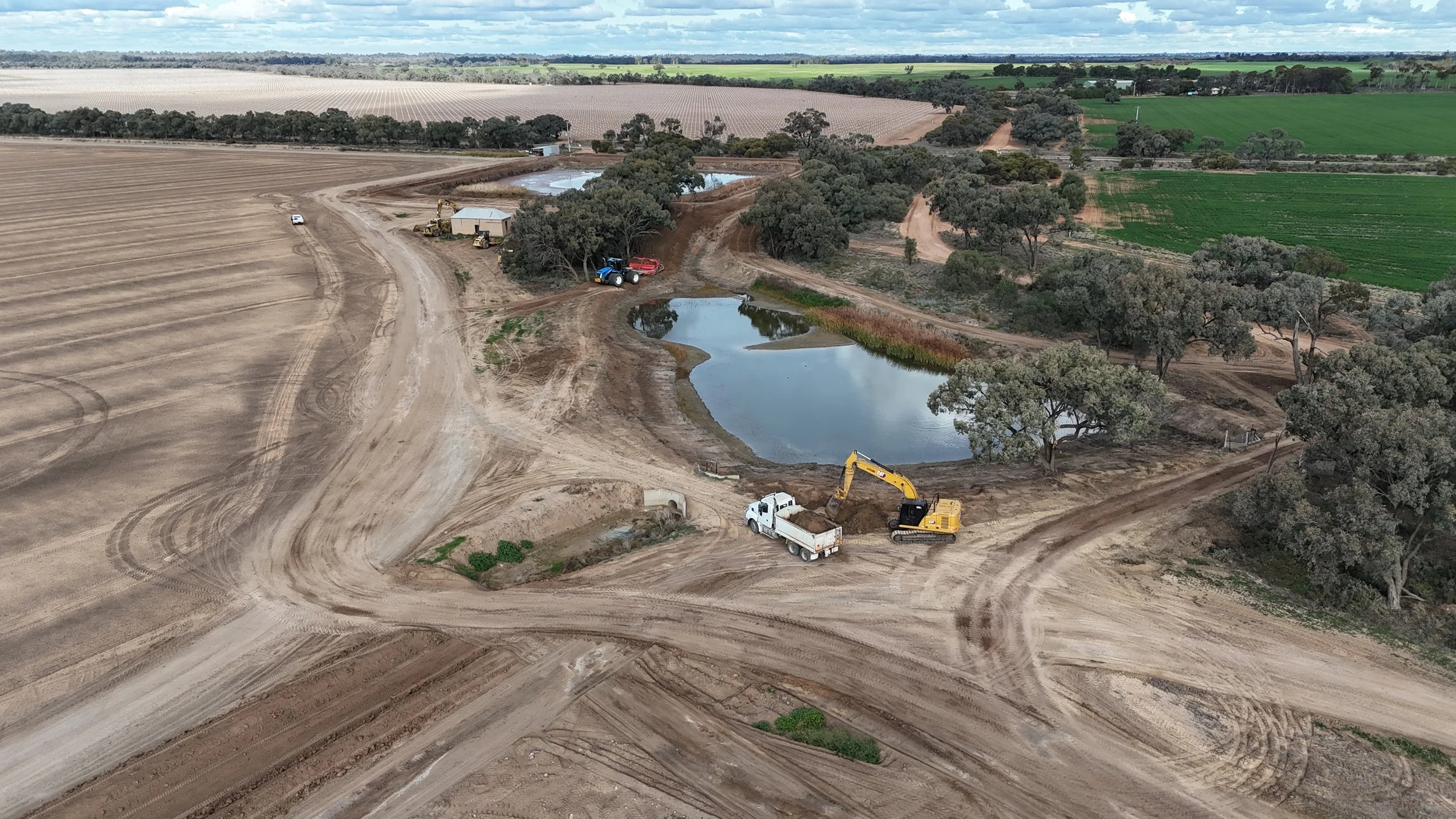 Aerial view of a farmland with construction site, machinery, and small ponds surrounded by trees and fields.