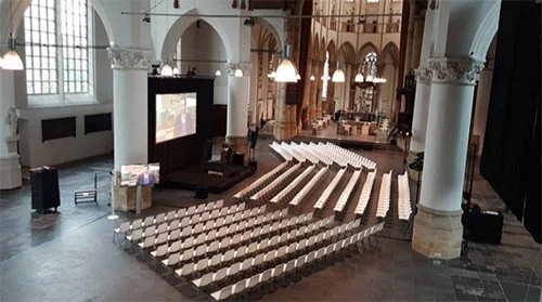 Grote zaal met rijen lege stoelen en een groot scherm, klaar voor een evenement of conferentie.
