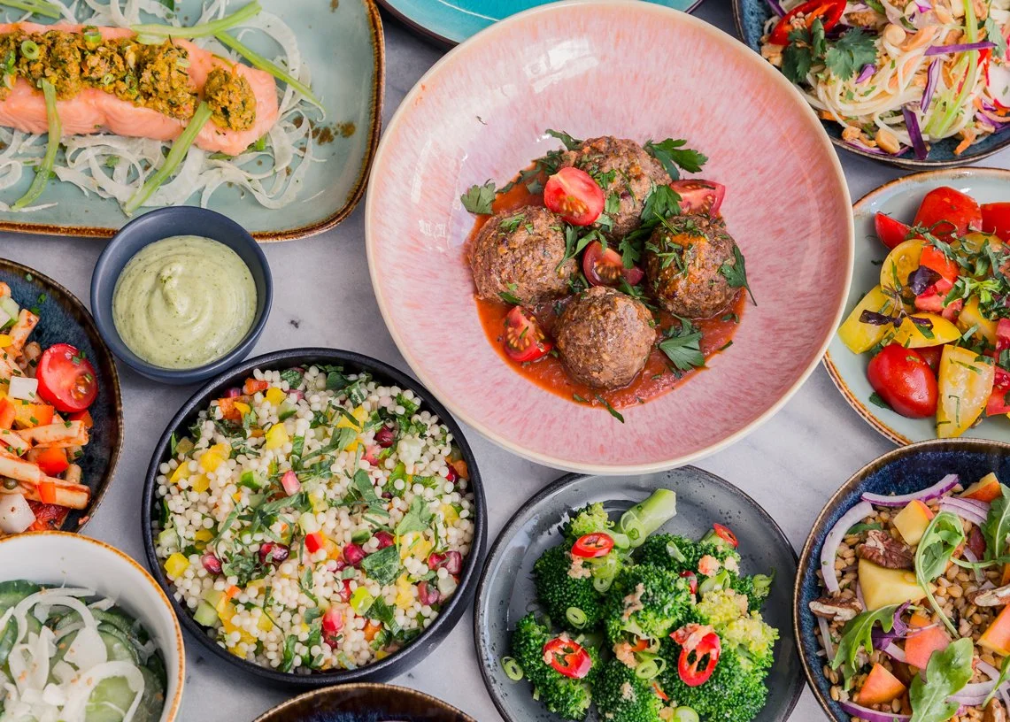 Een verscheidenheid aan kleurrijke Mediterrane gerechten op een tafel, waaronder salades, gehaktballetjes in saus, en dips.