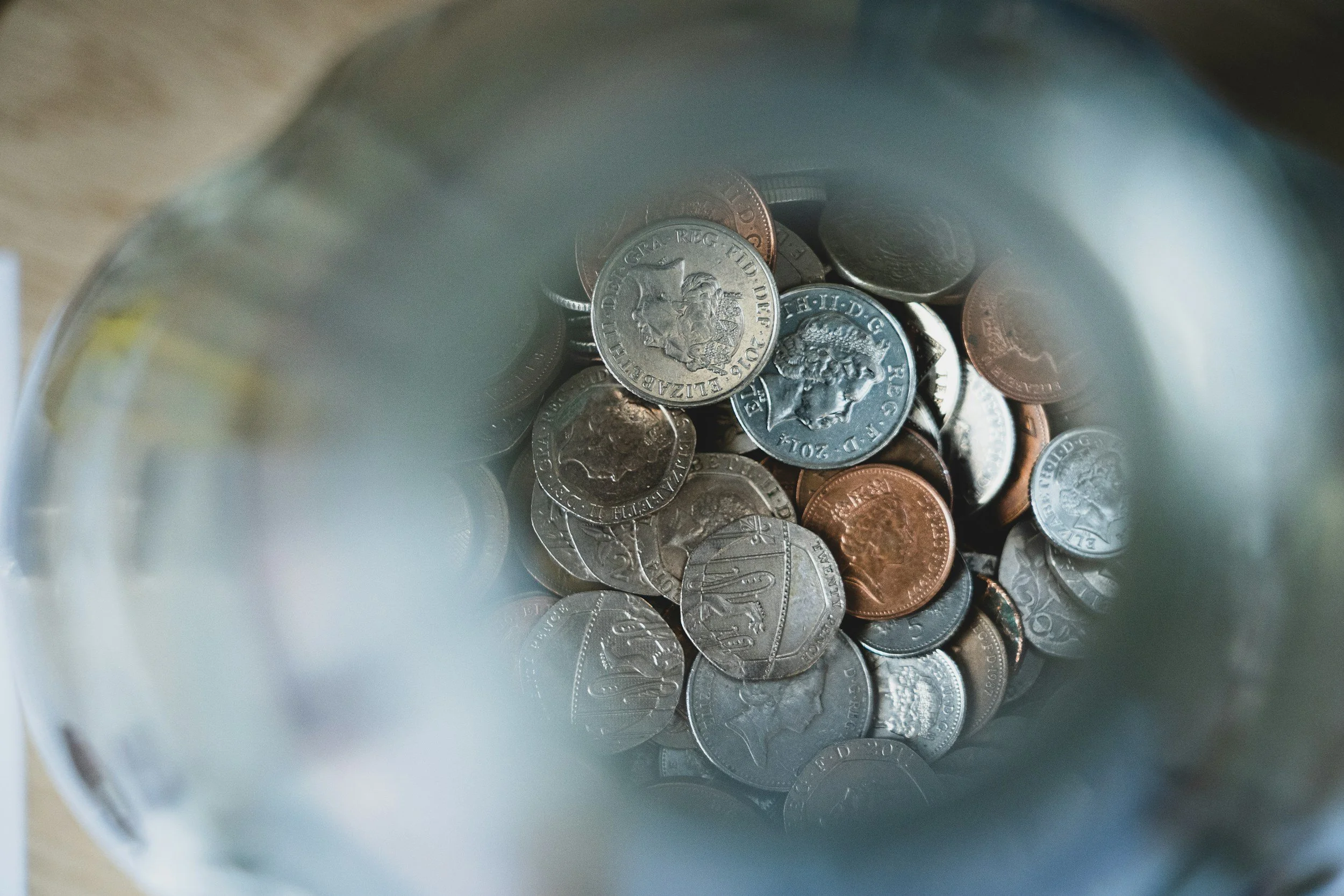 Looking down the top of an out of focus jug to a pile of British coins at the bottom