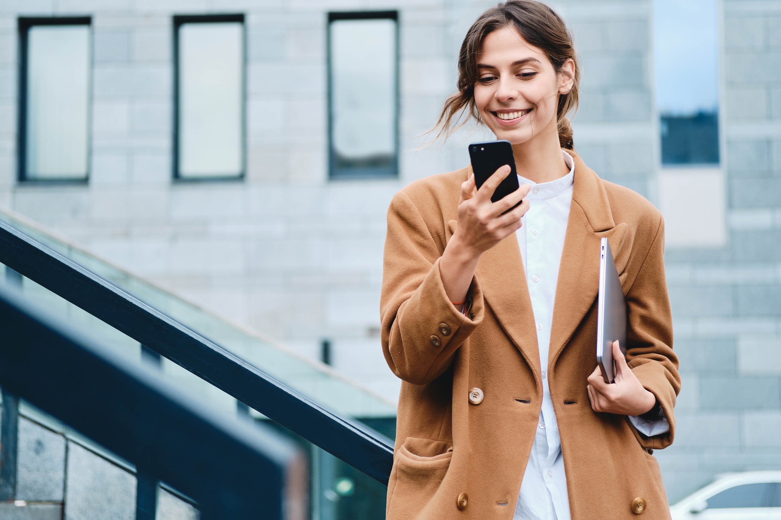  A woman wearing a coat and white shirt, holding a phone in her hand. 