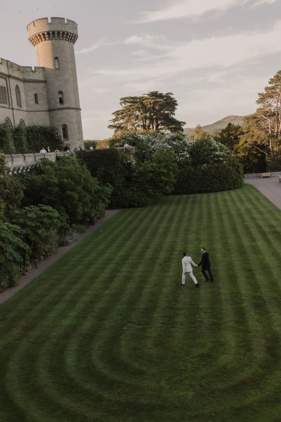 Vogue Wedding couple framed by dramatic castle architecture and landscaped gardens