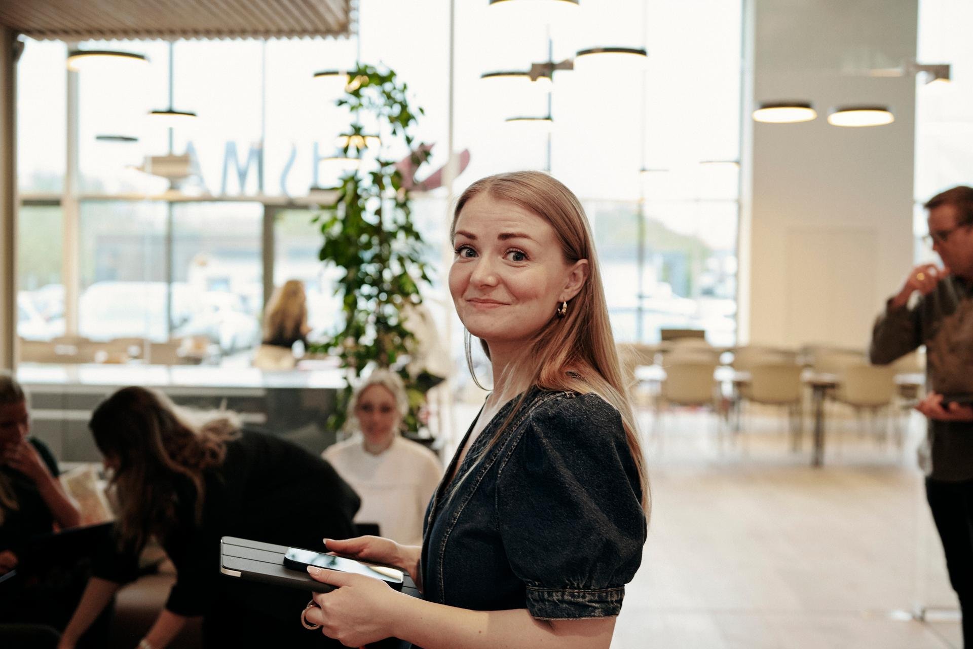 Bilde av en kvinnelig ansatt med en iPad og en telefon med mennesker i bakgrunnen.