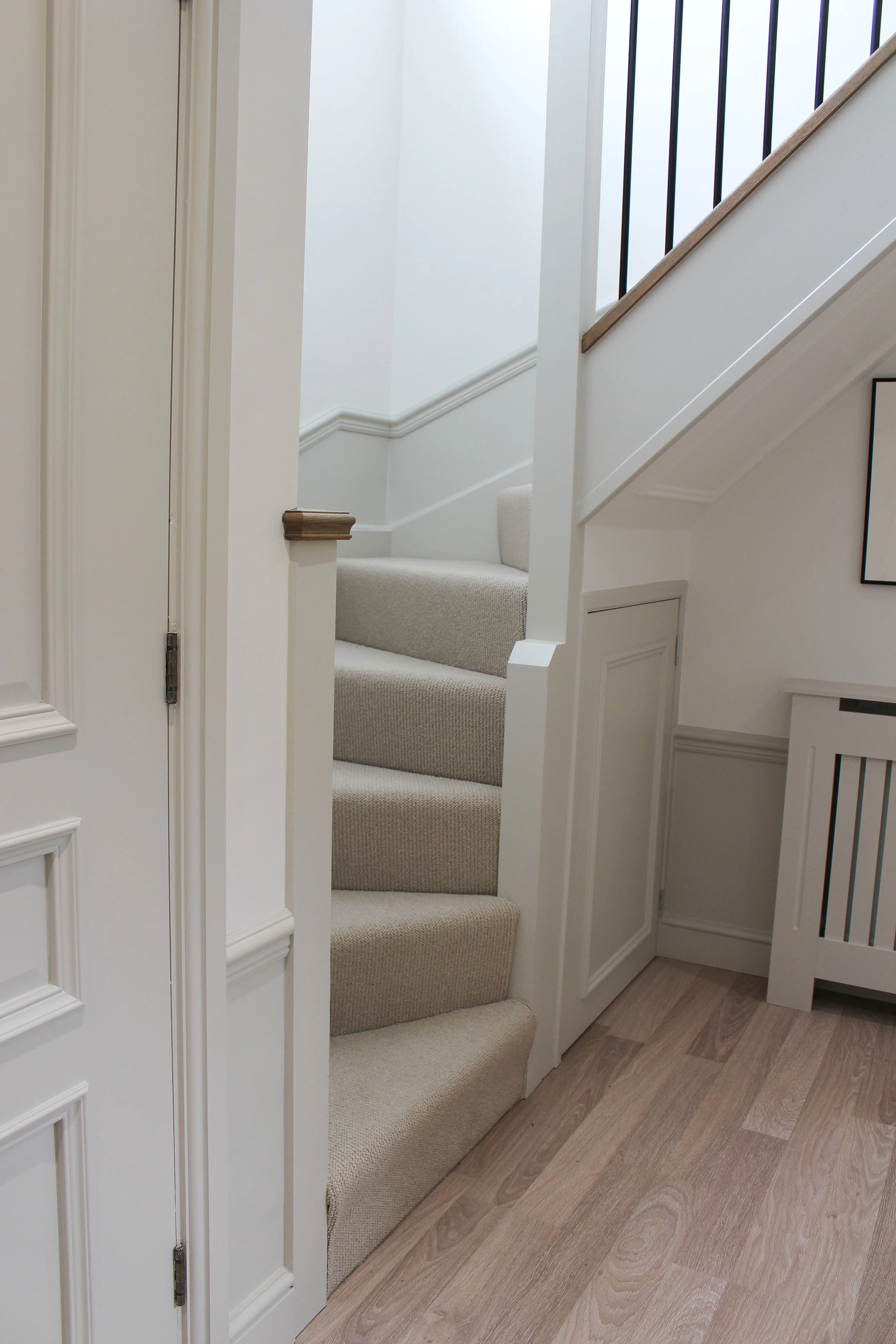 Interior view of a staircase with carpeted steps, white walls, and wooden and black metal handrails.