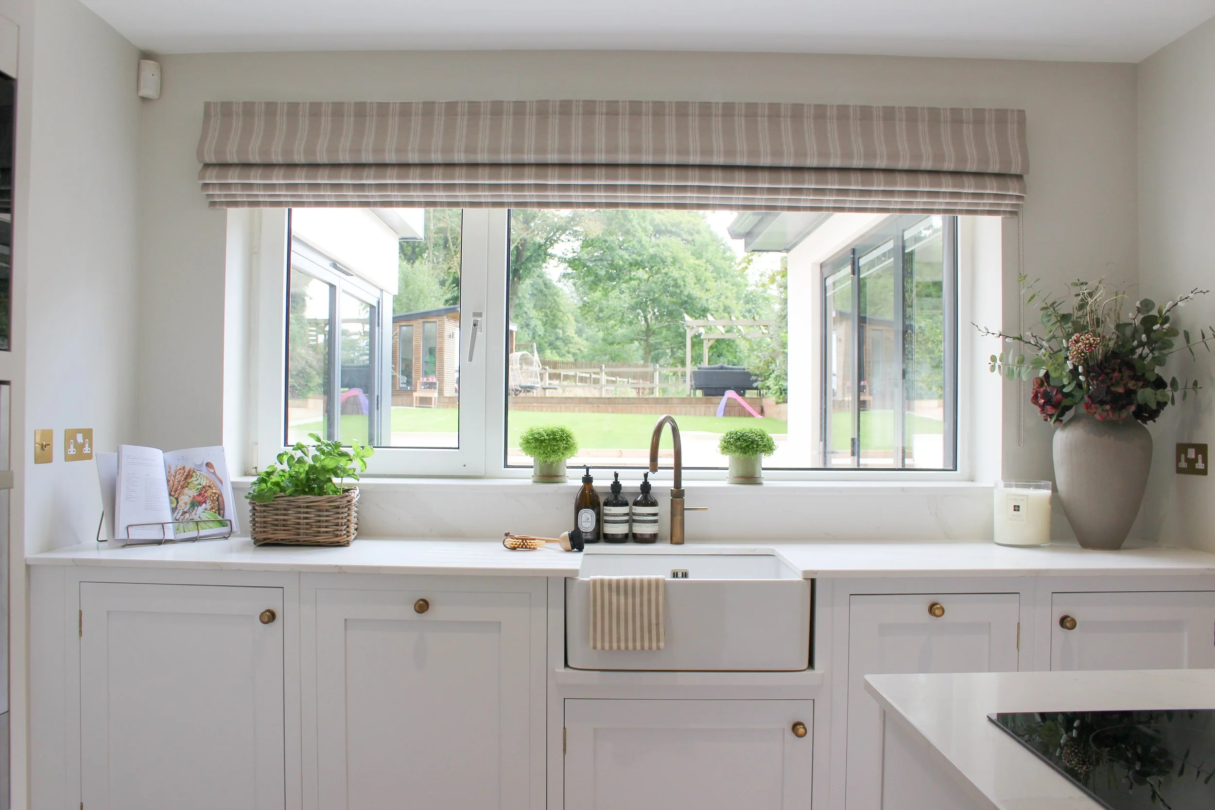 A bright kitchen with a window looking out to a backyard garden, white cabinets, and a farmhouse sink with a striped towel hanging on the front.