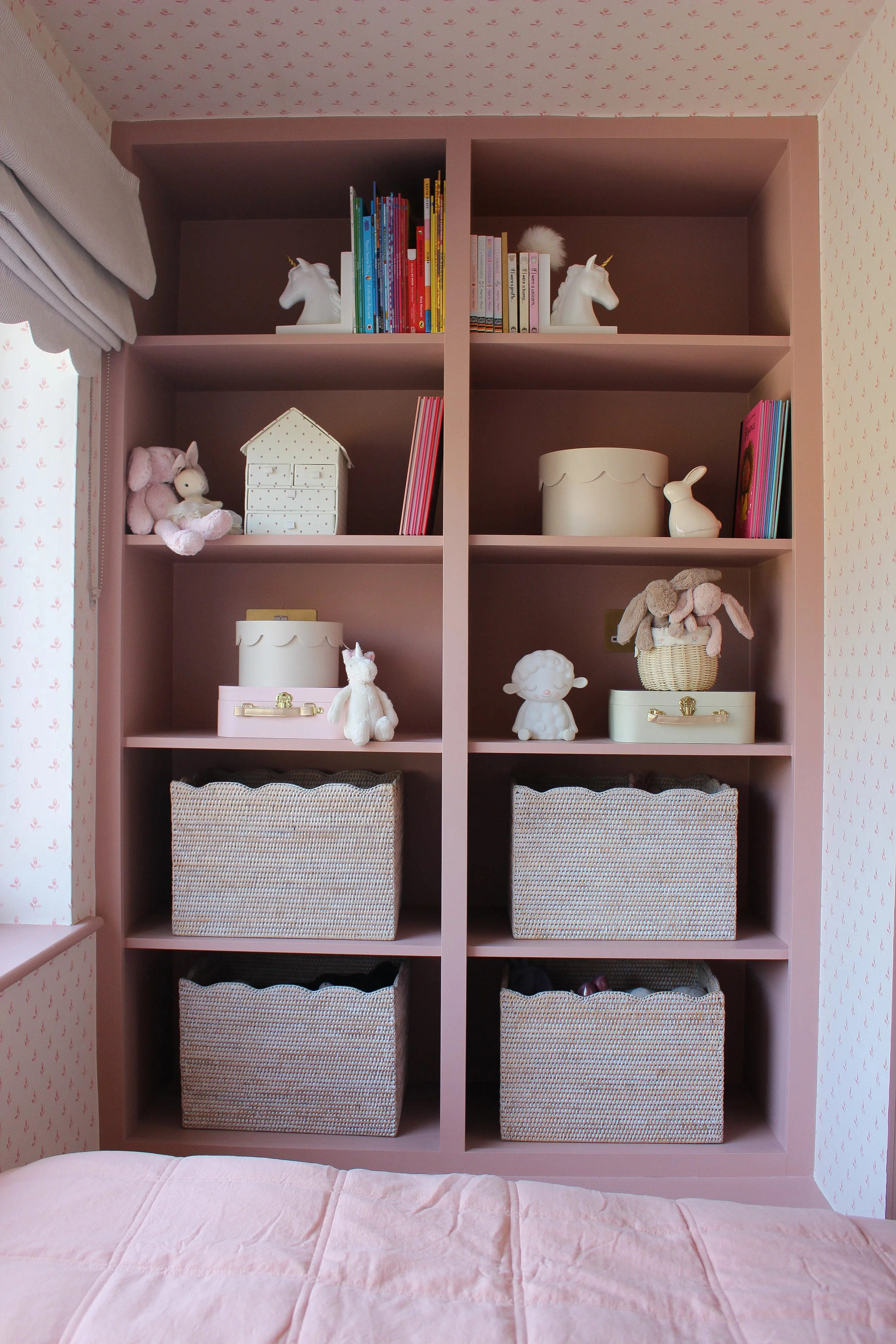 Pink bookshelf with children’s toys and books, including stuffed animals, unicorn figurines, and decorative storage boxes. Girls bedroom designed by Yazzmin Lovelle Interiors