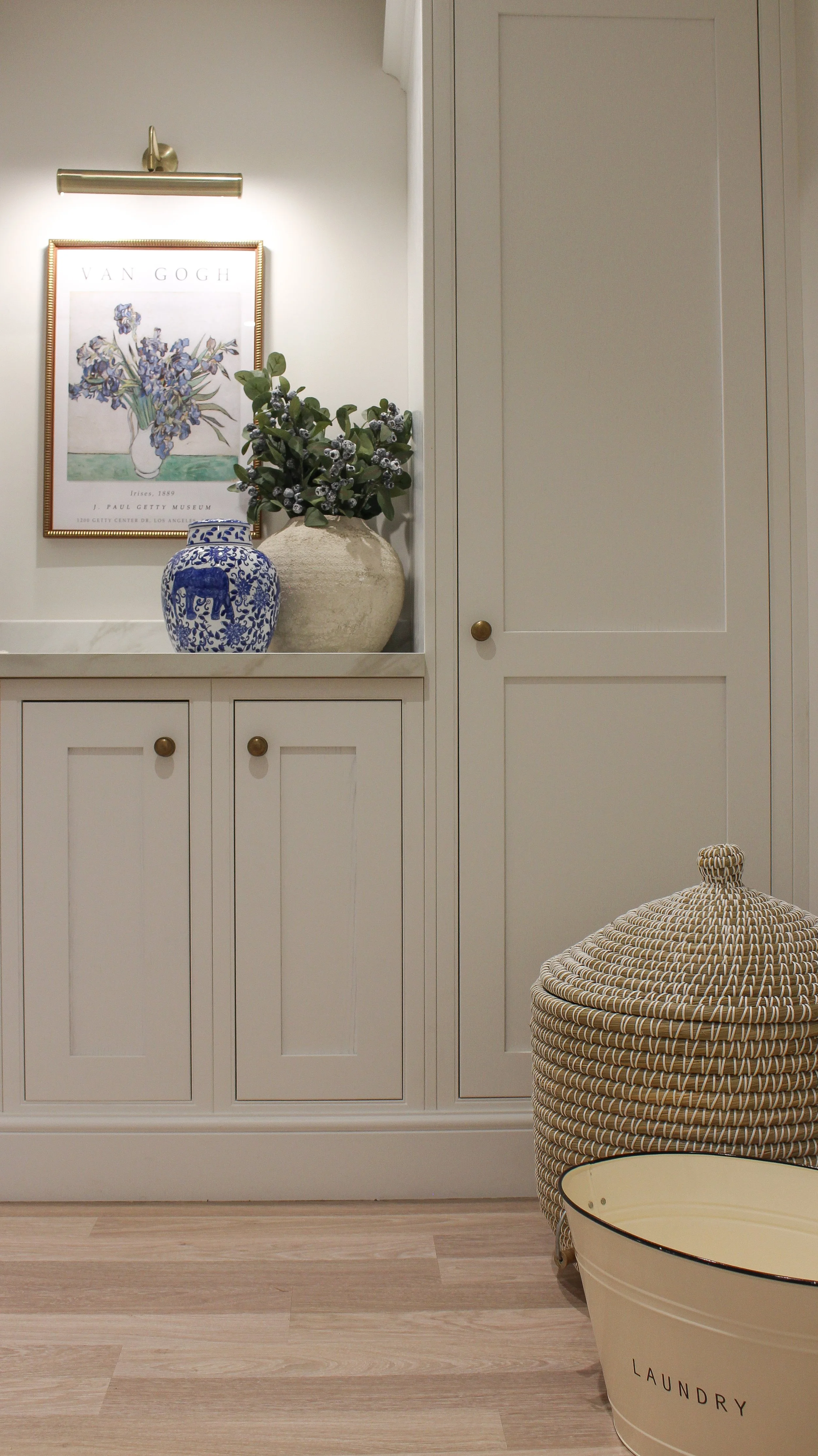 Decorative interior space featuring a framed Van Gogh art print, two vases with flowers, a woven laundry basket, and a laundry tub.