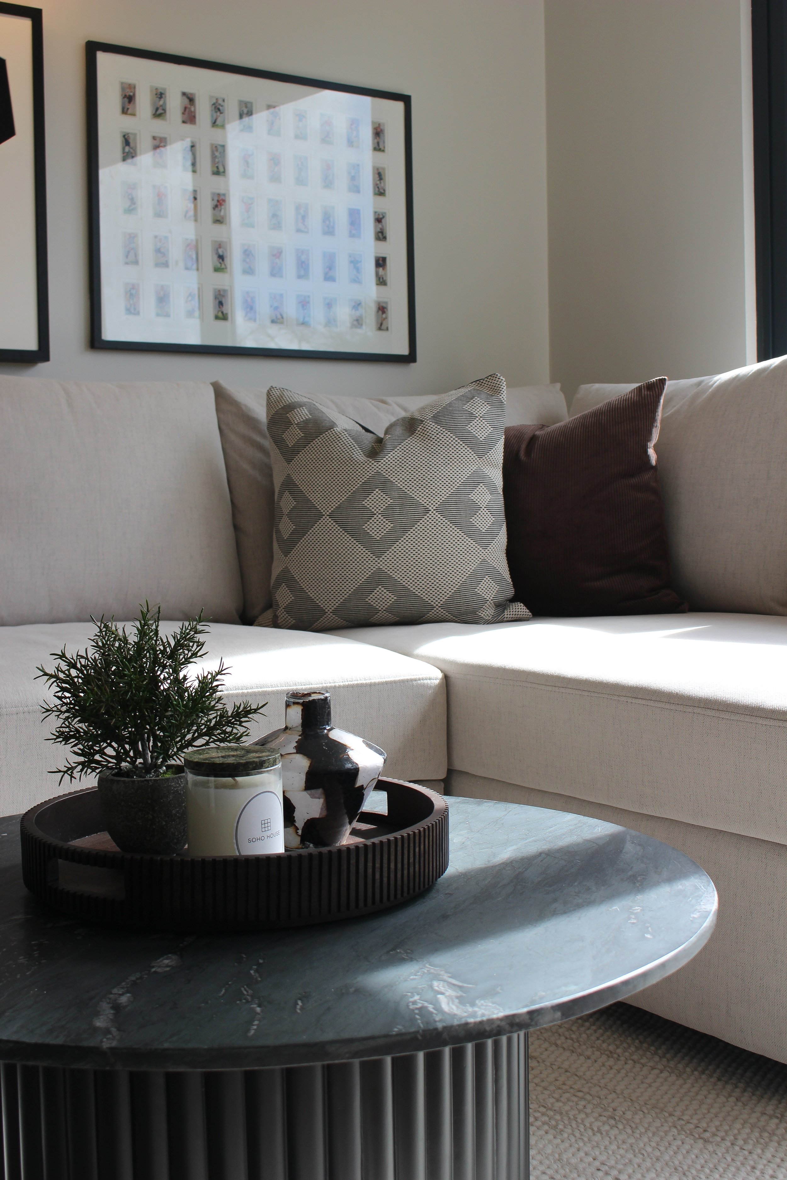 A modern corner of an office with a beige sectional sofa decorated with patterned and solid pillows, a marble coffee table with decorative items including a small plant, a candle, and a black and white vase. Office designed by Yazzmin McDonagh. 