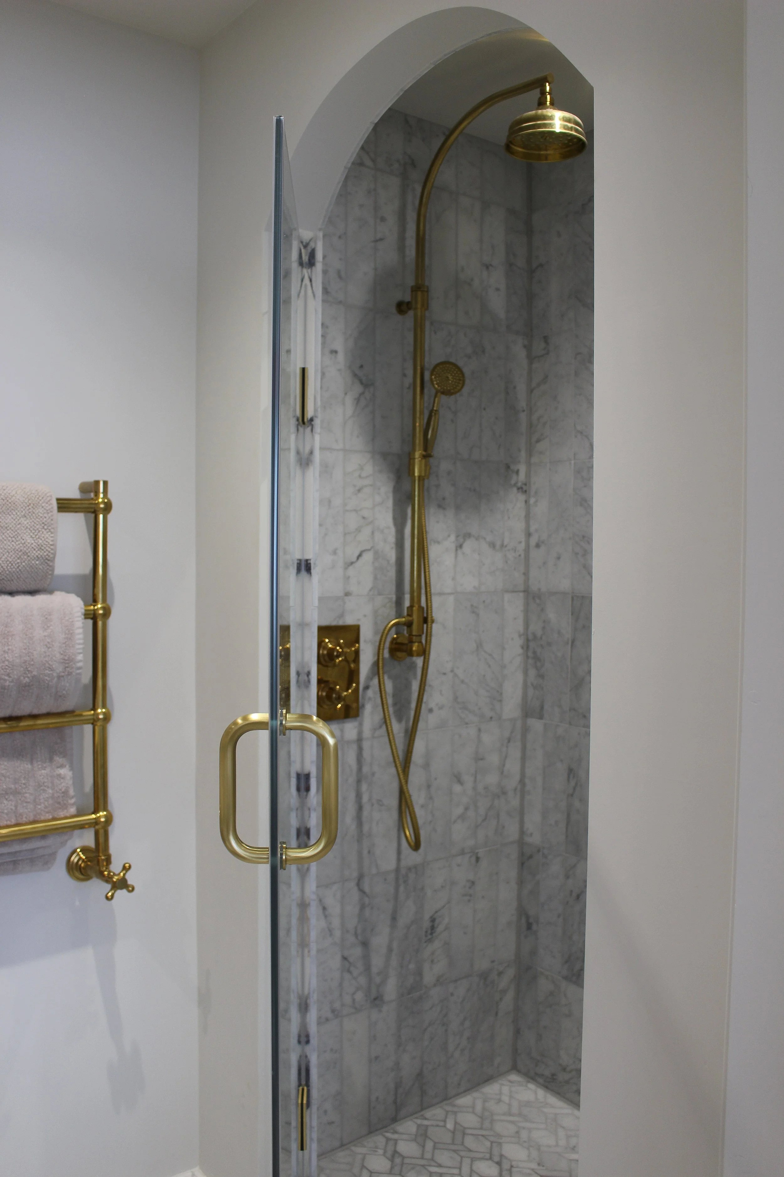 Arched Shower with marble tiles and brass fixtures in a bathroom. Master ensuite designed by Yazzmin Lovelle Interiors