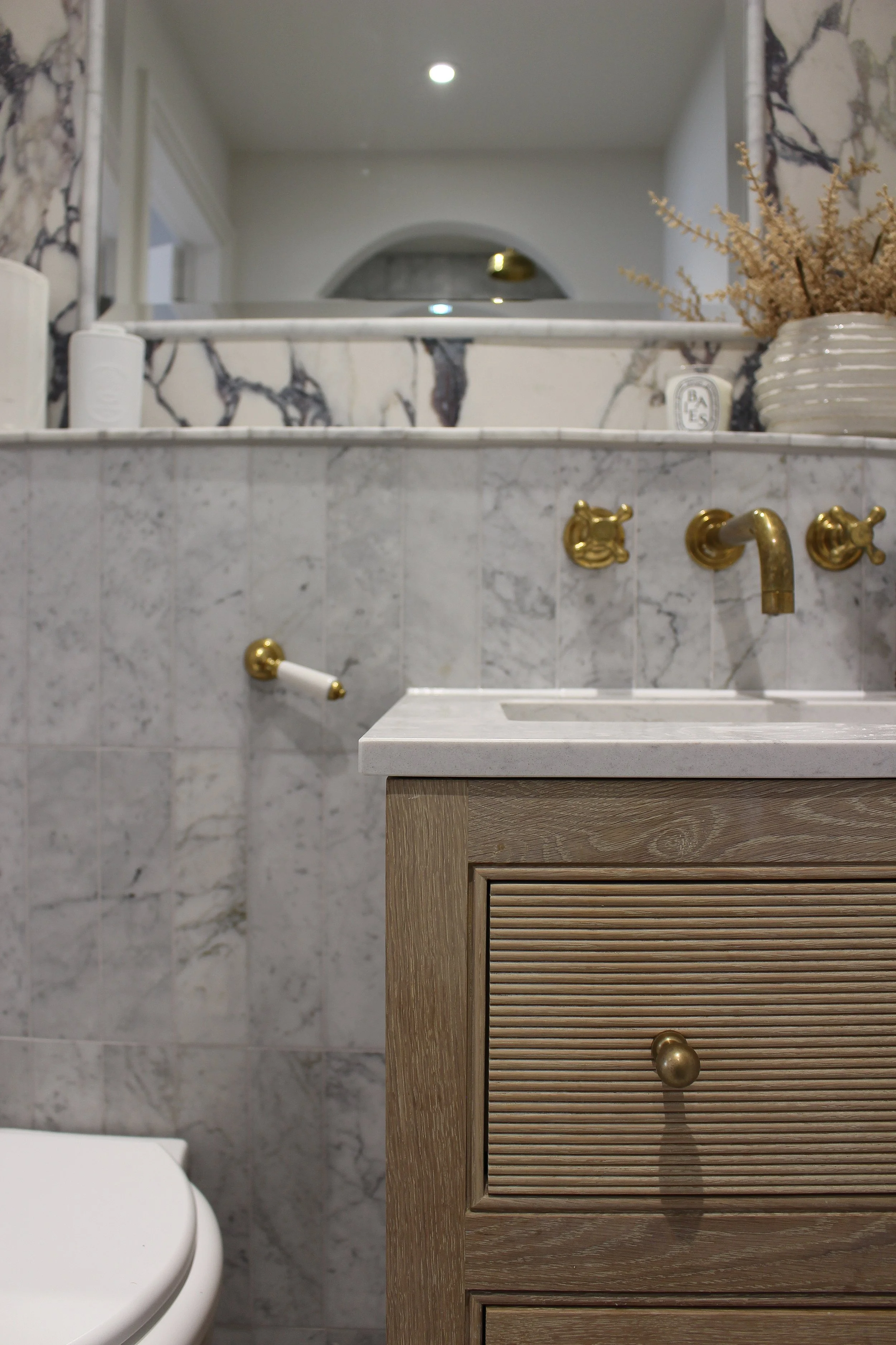 Close up of a bathroom vanity with antique brass fixtures, a marble countertop, and a wooden cabinet. Master ensuite designed by Yazzmin Lovelle Interiors
