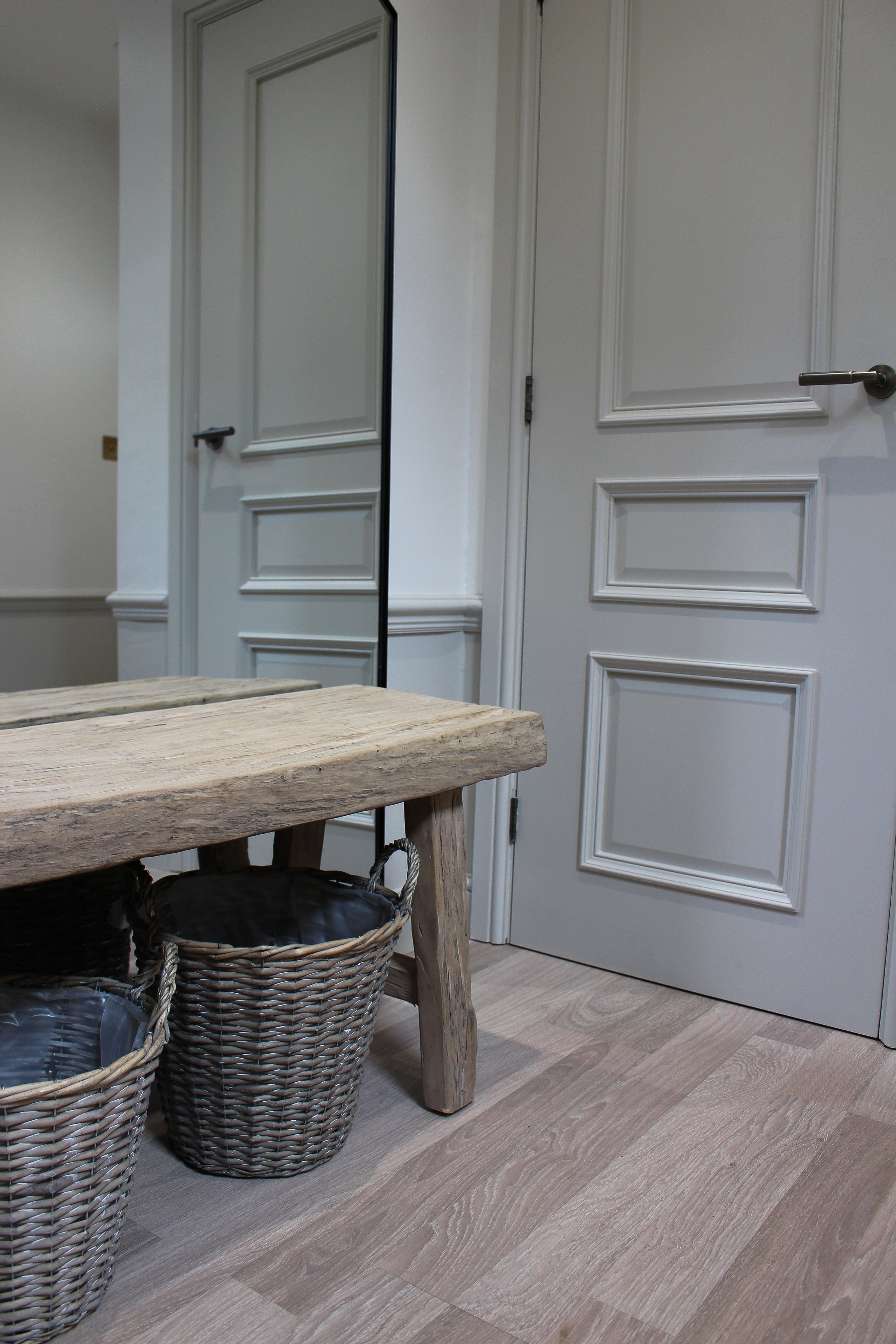Interior room with white panelled doors, a rustic wooden bench, and woven baskets on a light wood floor. Hallway designed by Yazzmin Lovelle Interiors 