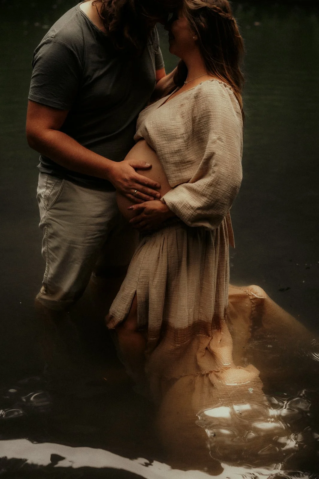 Eine schwangere Frau und ein Mann stehen im Wasser und küssen sich; natürliche Fotografie in Melle