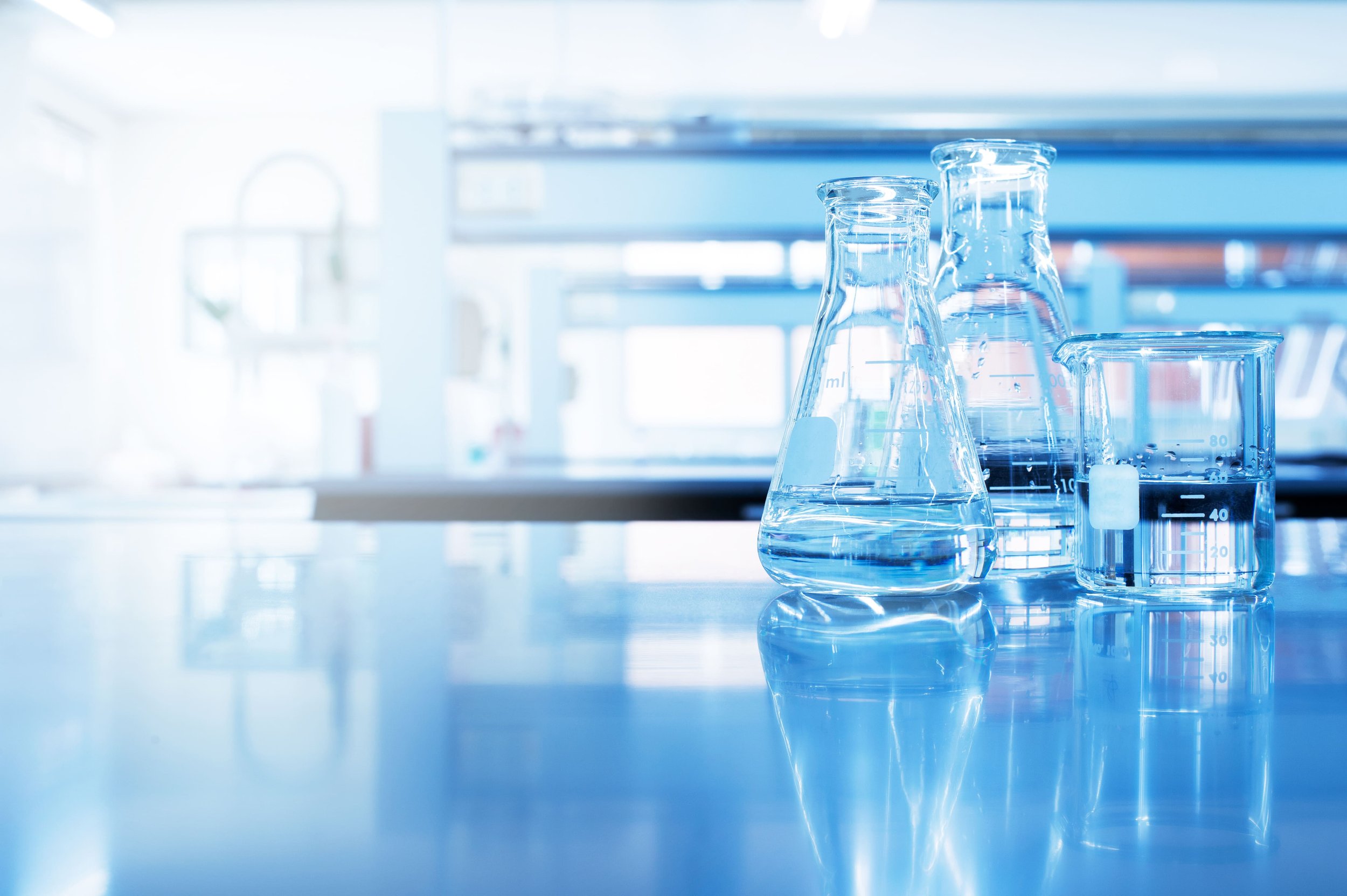 Hands holding a glass container with blue liquid and using a pipette to add more liquid into it.