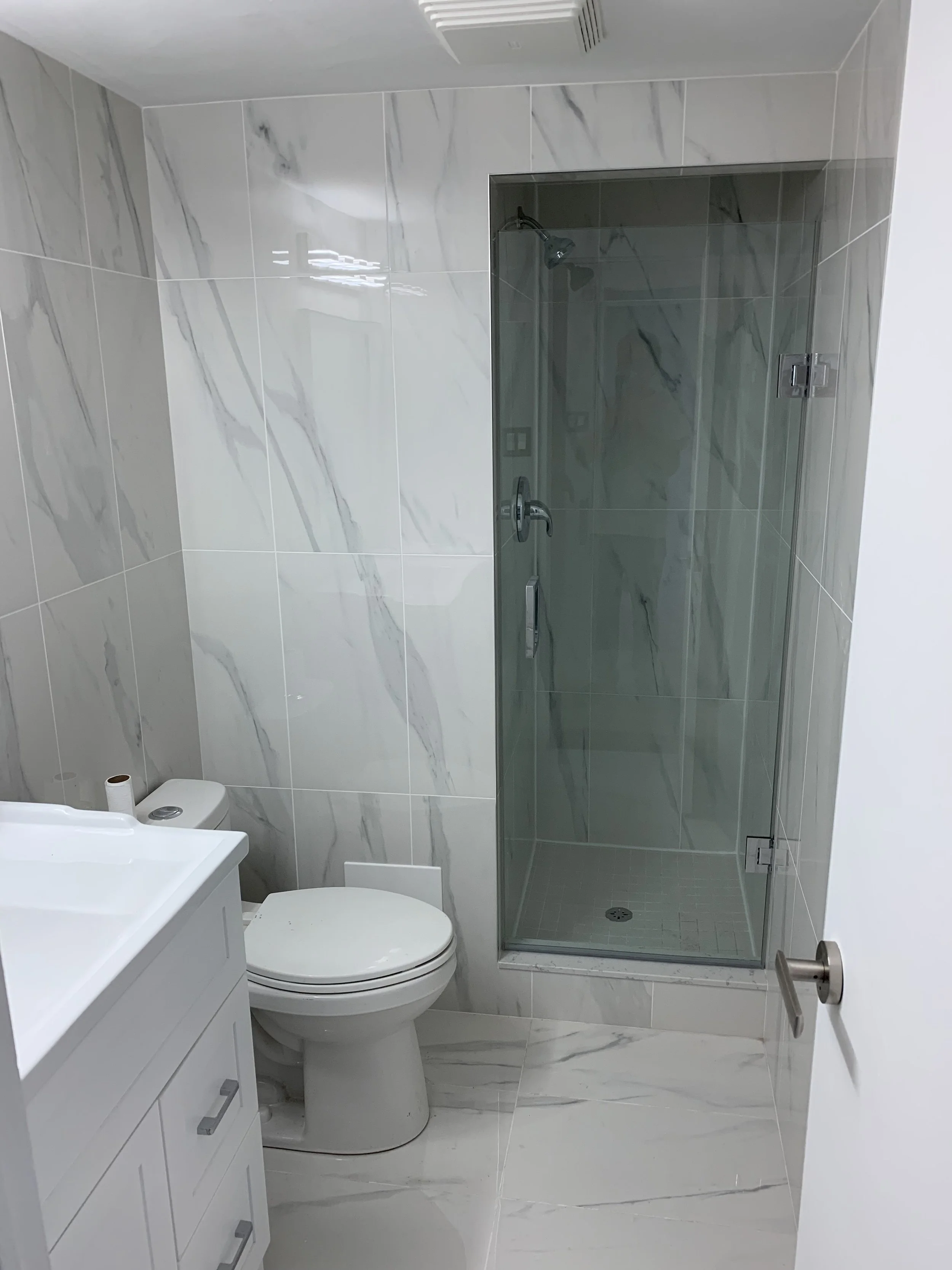 Remodelled white bathroom with matching floor and wall tiles including a walk in shower