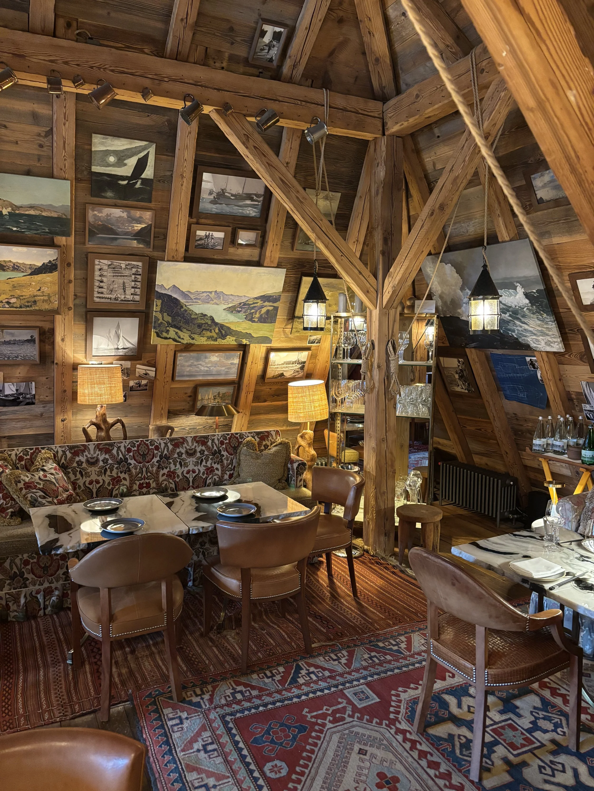 Rustic A-frame chalet dining room at La Muna in Switzerland, filled with vintage sailing art and warm lantern lighting
