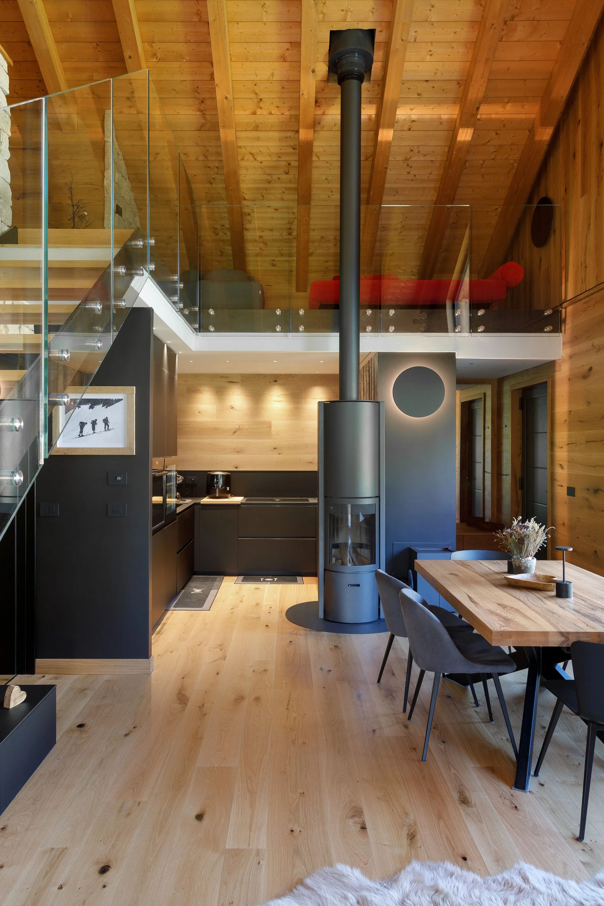 Interno di una casa in stile rustico con pareti e soffitto in legno, cucina moderna nera con camino in metallo, tavolo in legno circondato da sedie grigie, decorazioni minimaliste, pianeta Terra in ceramica, una pianta in vaso sulla tavola, pareti co