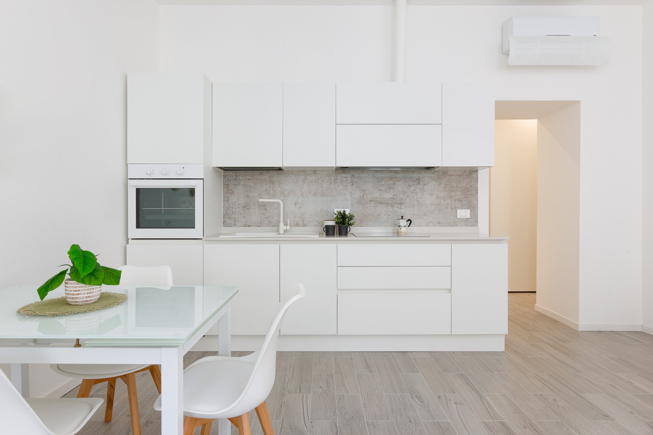 Cucina moderna con mobili bianchi, tavolo con sedia, pianta decorativa sul tavolo, forno integrato e piano da lavoro con lavello.