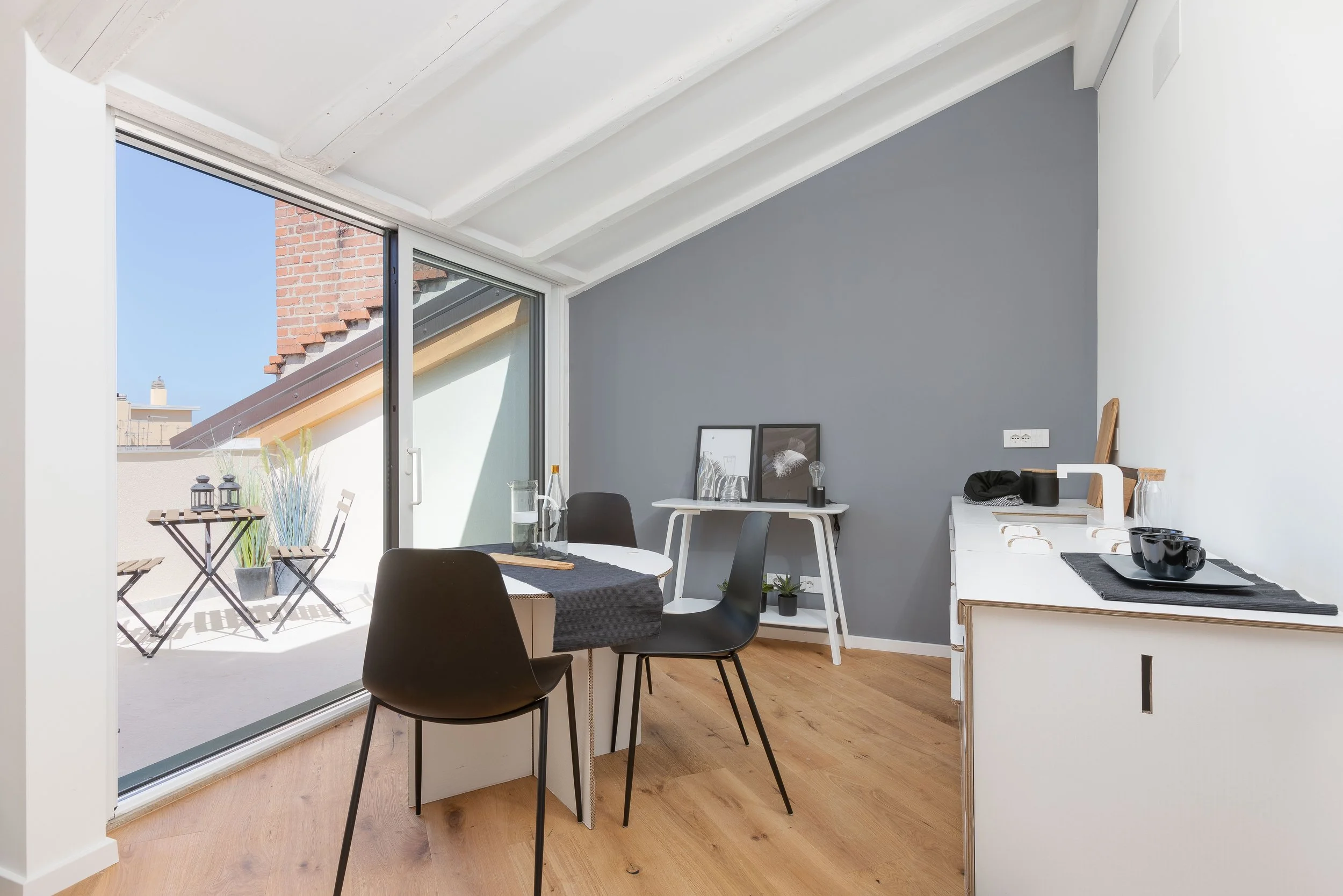 Interno di un soggiorno con grandi finestre che danno su un balcone all'aperto, arredi moderni, e pareti di colore grigio e bianco.