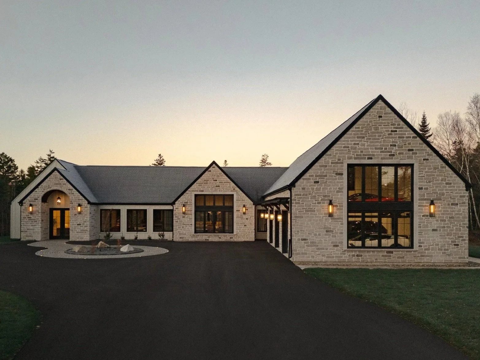Modern two-story house with mixed exterior siding and stone accents, black-framed windows, a small front porch with black railing, and a well-kept lawn, surrounded by trees.