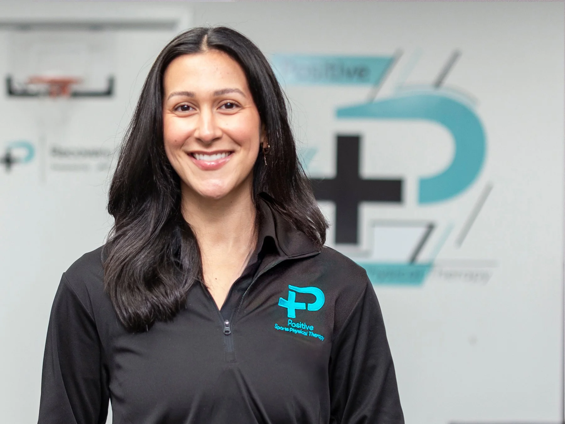 A light skinned, dark haired woman standing against a white wall