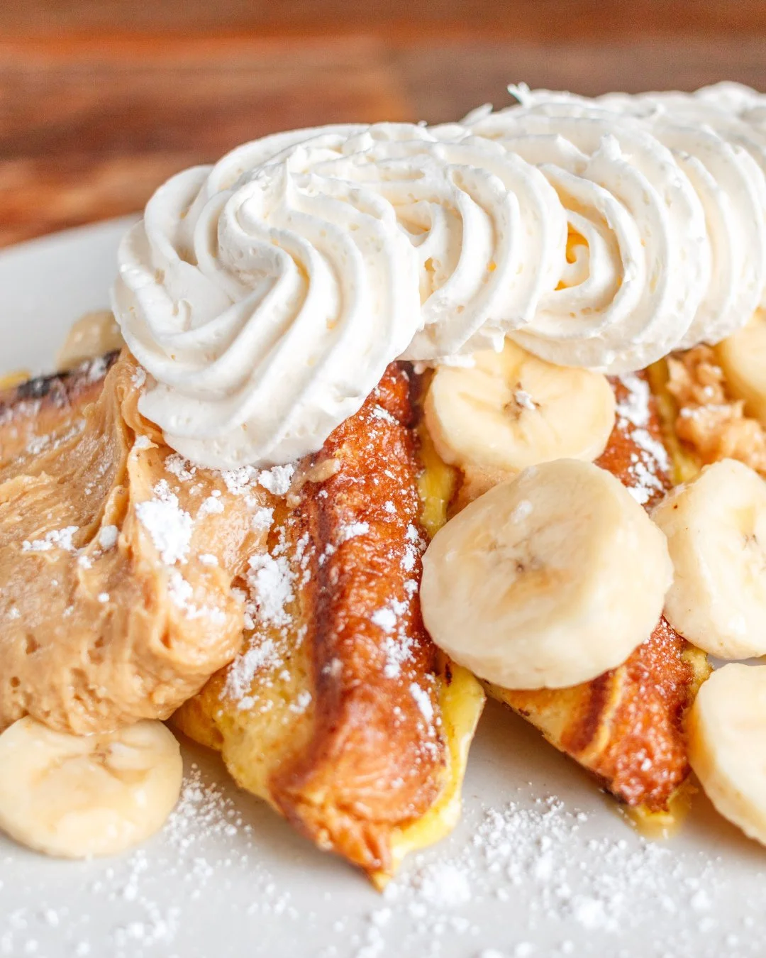 Saturday mornings were made for this. 👑🍌 The King's French Toast is stacked with peanut butter-cream cheese fluff, fresh bananas, whipped cream and a dusting of powdered sugar. Sleep in, then come hungry.