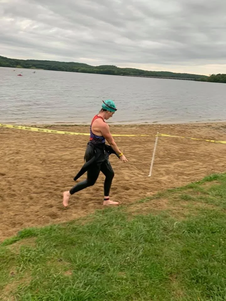 An athlete running up the beach with a wetsuit half off