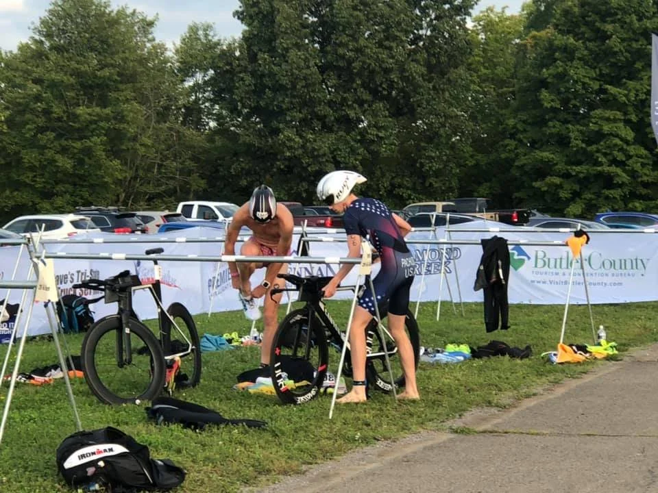 Athletes putting on shoes beside their bikes in transition