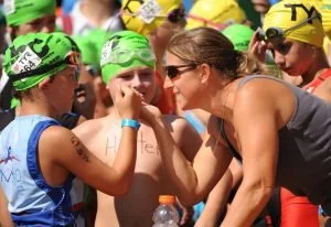 Joella Baker kneeling with young athletes in swim caps at a race
