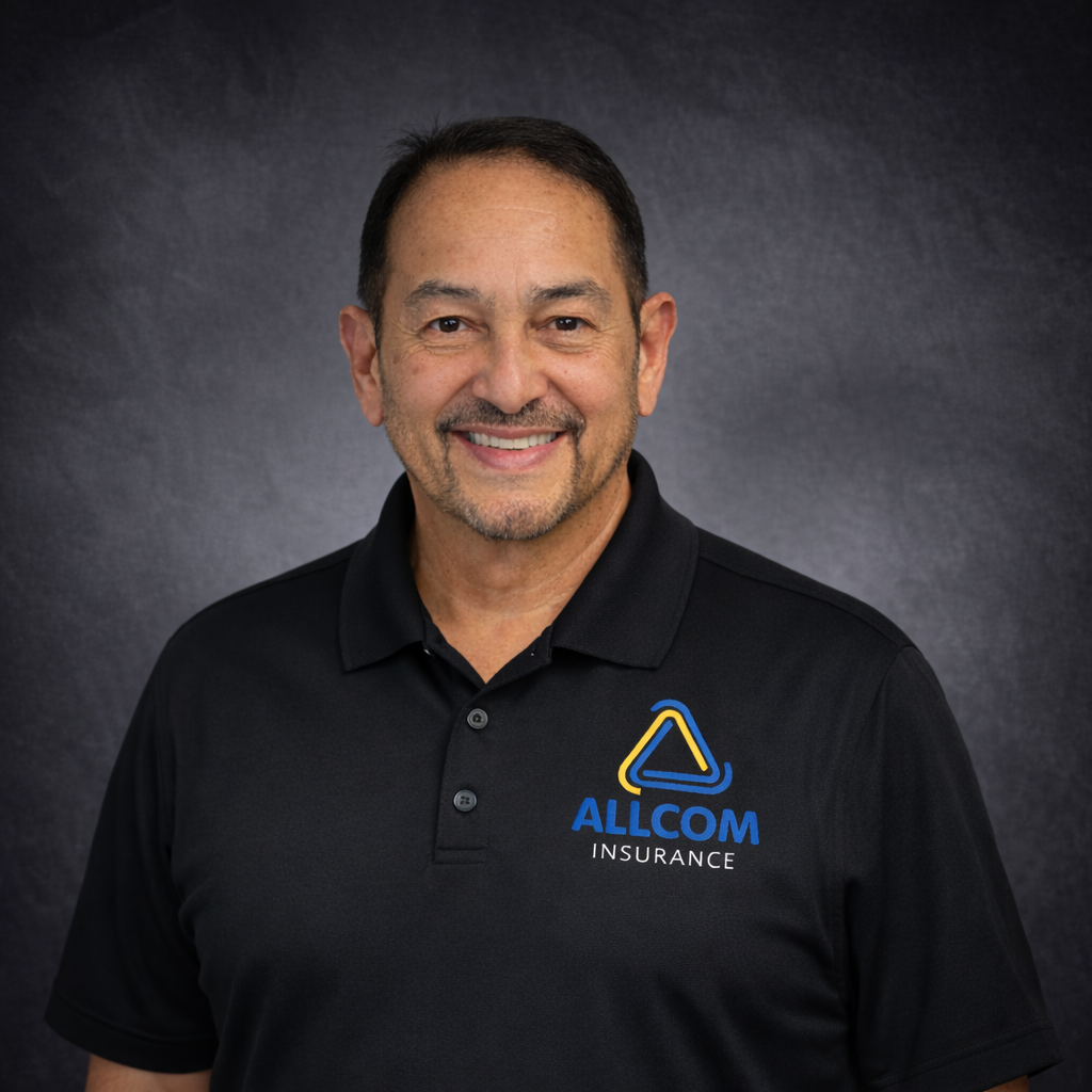 A man smiling, wearing a black polo shirt with the Allcom Insurance logo on it, against a dark gray background.