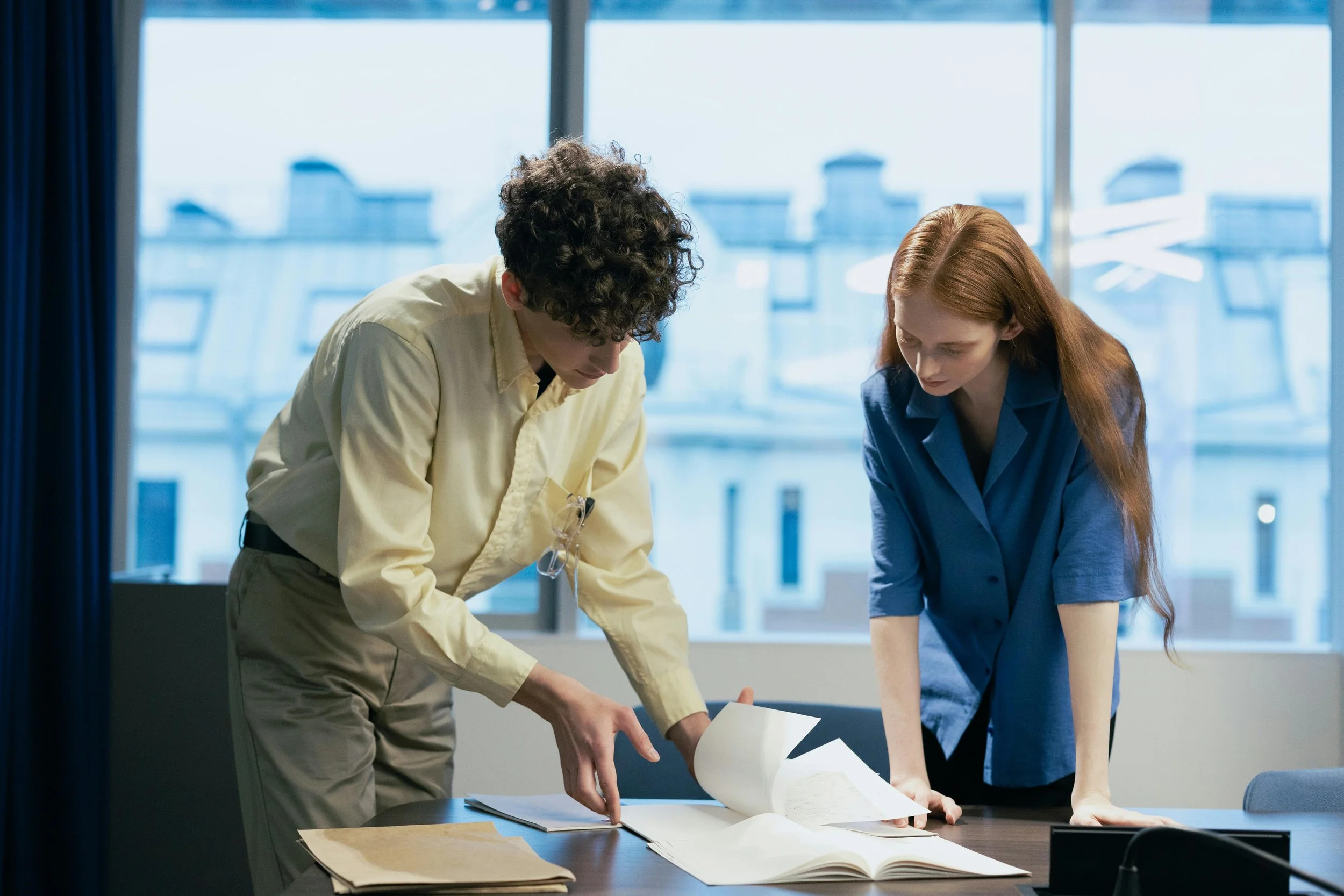young man in yellow shirt and woman with long hair looking at paper documents together in an office setting