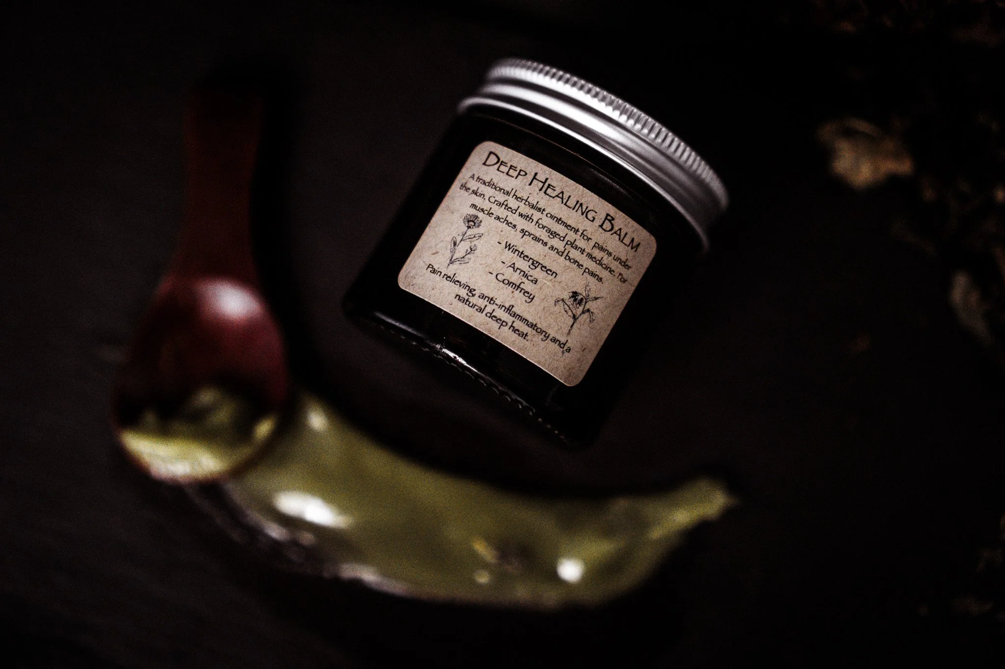 A dark jar of Deep Healing Balm on a black surface, with a small ceramic dish and an apple in the background.