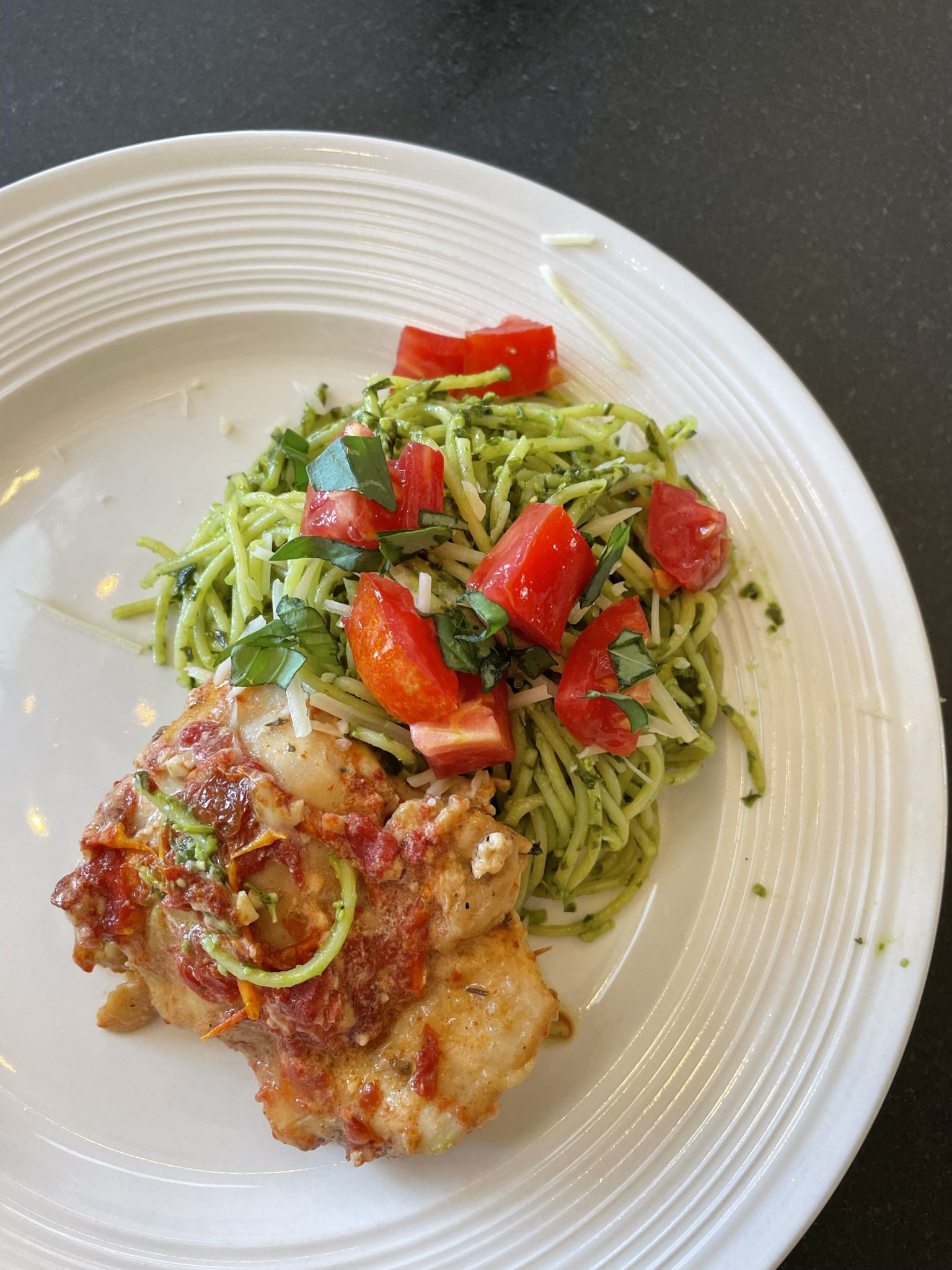 A white plate with a pasta dish featuring spaghetti topped with chopped tomatoes and basil, with a side of fried chicken with tomato sauce.
