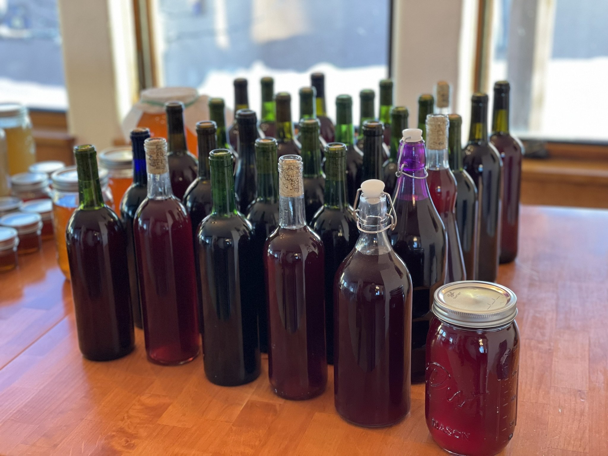 Various bottles and jars, some with cork stoppers, filled with colorful liquids, arranged on a wooden table near a window.