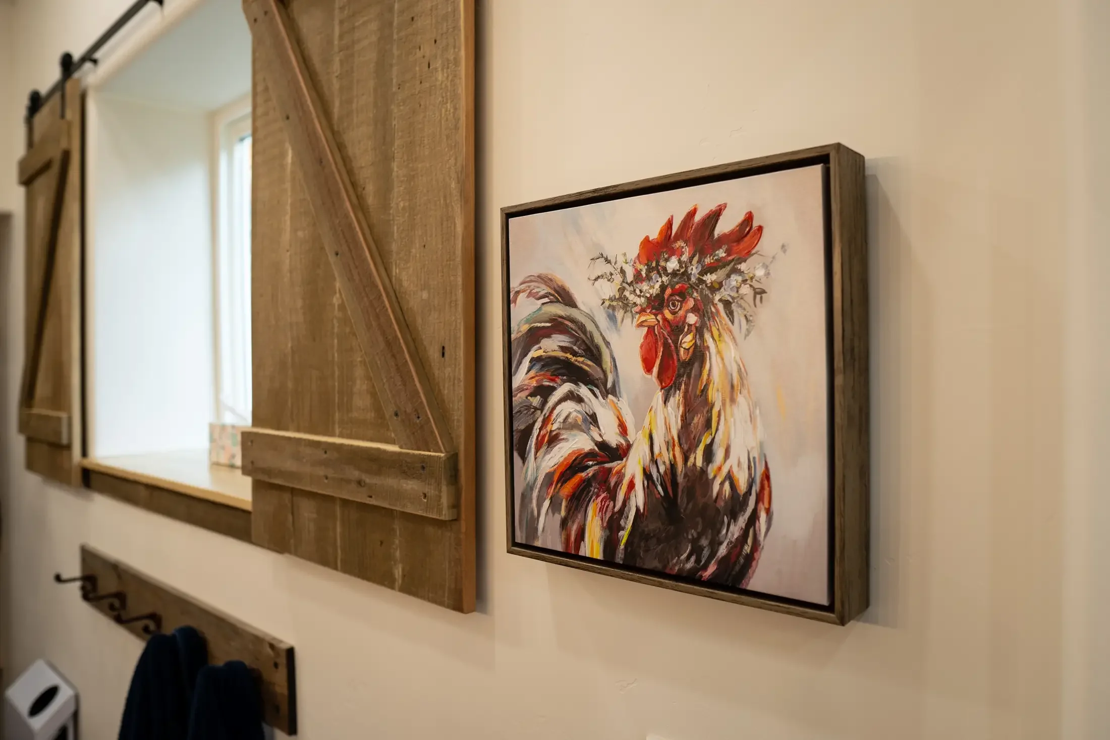Interior of a house with framed artwork of a colorful rooster, mounted on a wall next to wooden barn-style sliding doors.