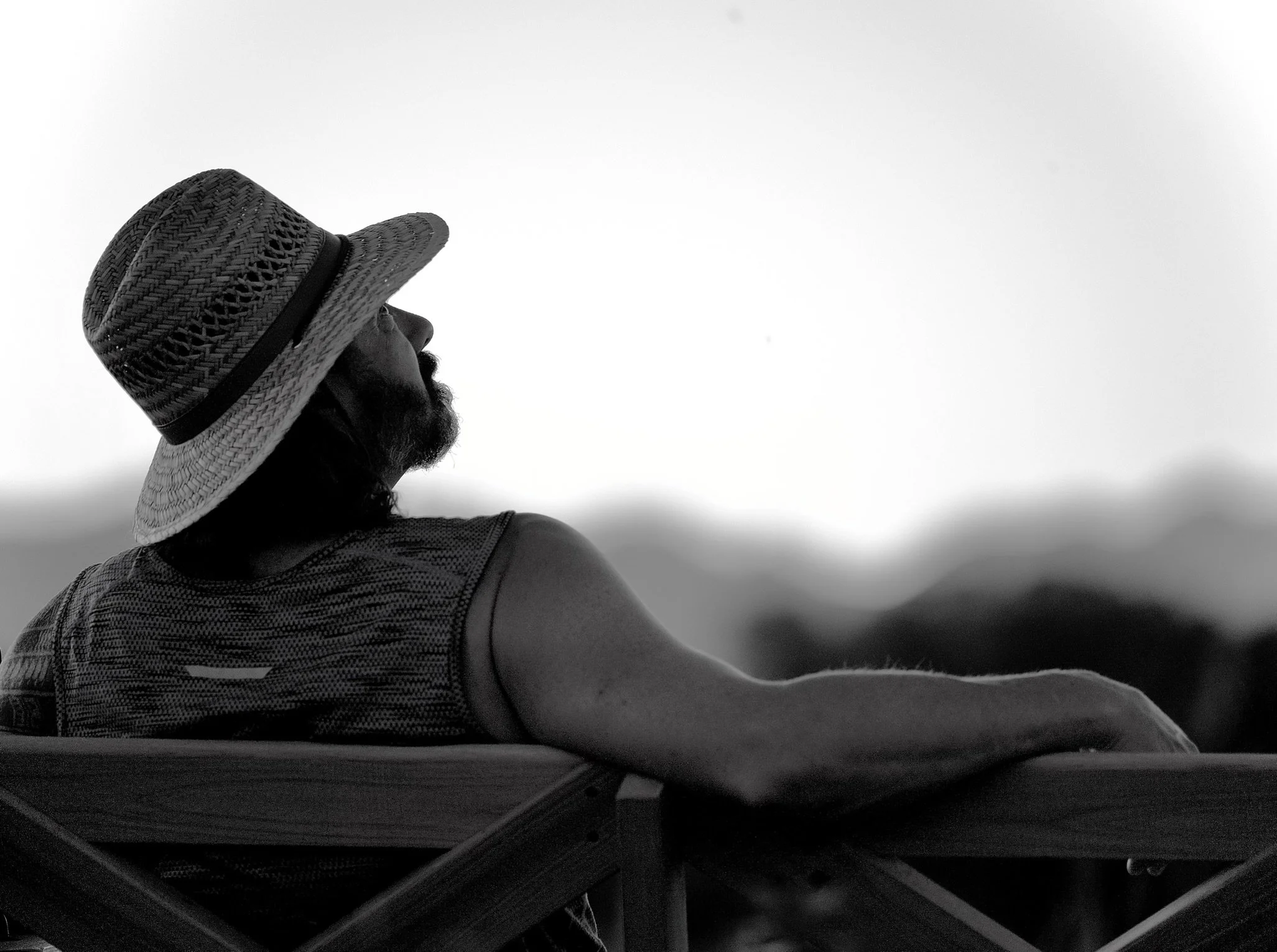 A person wearing a wide-brimmed hat and a sleeveless top, standing outdoors against a cloudy sky.