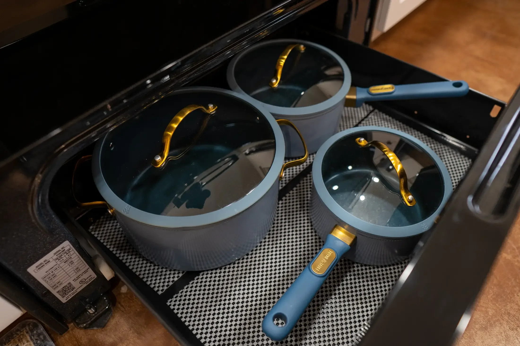 Three blue and gold saucepans with glass lids inside a black oven.