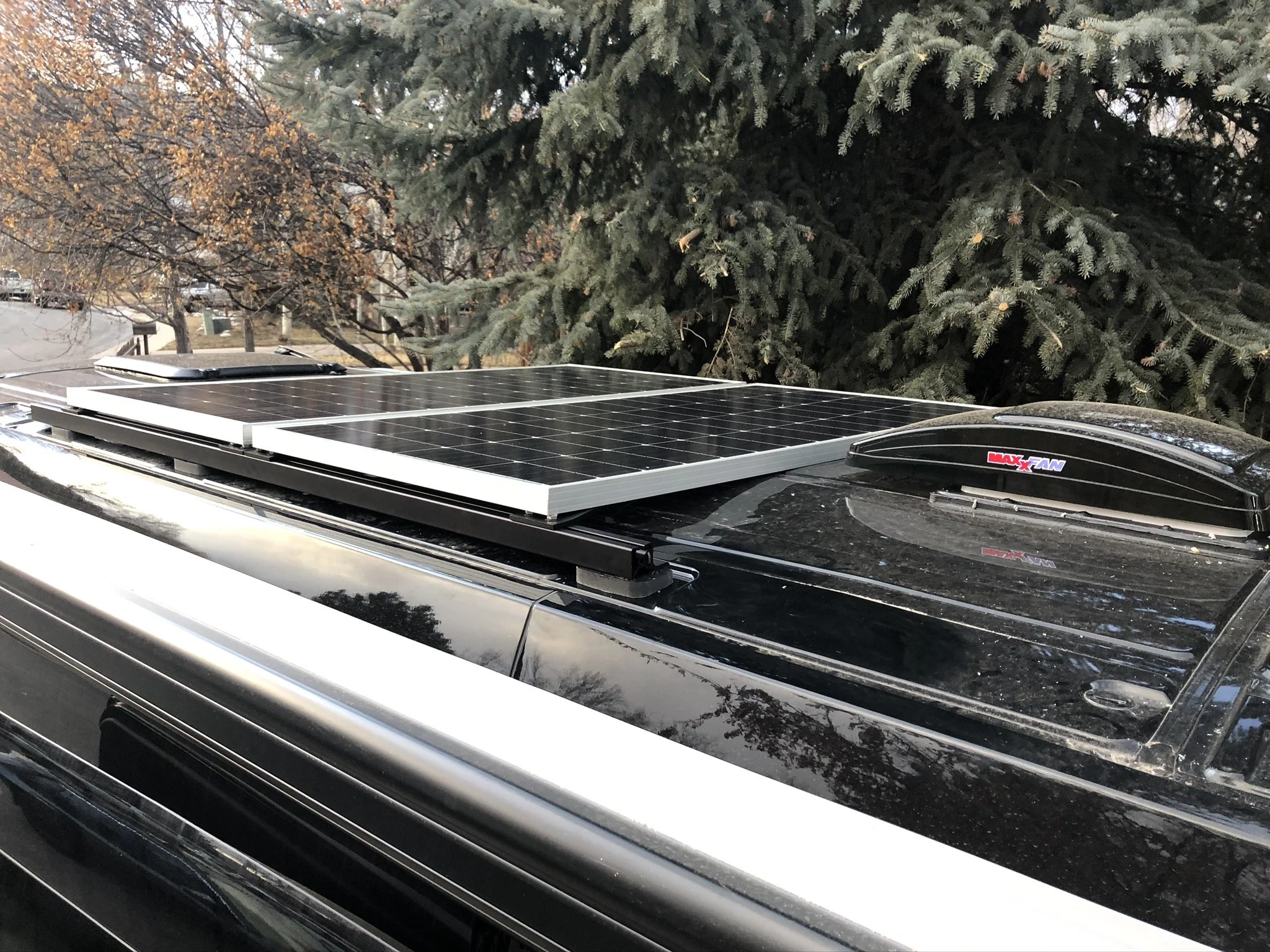 Car roof with solar panels installed, set against a background of trees with green and orange leaves.