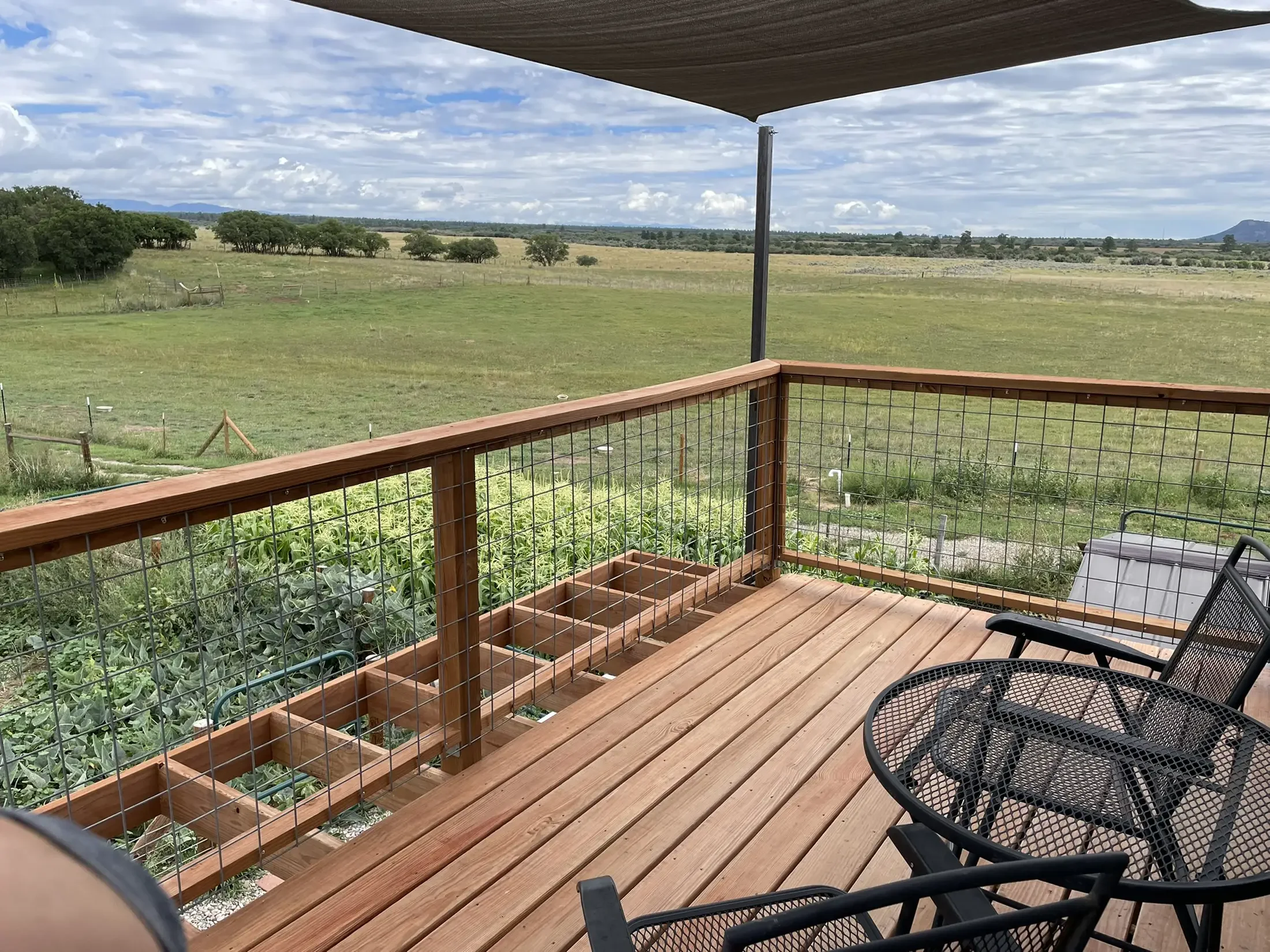View from a wooden balcony overlooking a vast grassy field with scattered trees and distant mountains under a partly cloudy sky.