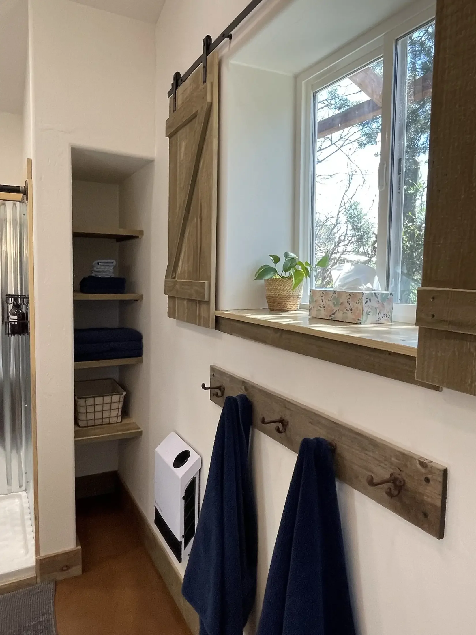 Bathroom with wooden shelf and hooks, towels hanging, window with a potted plant and tissue box, laundry hamper, and laundry machine.