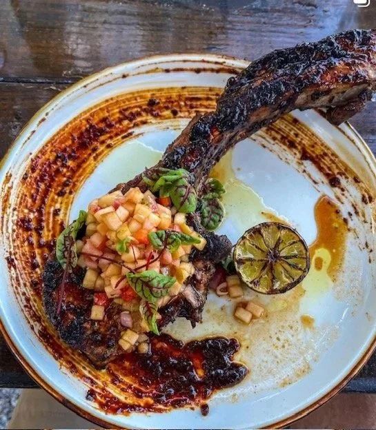 Grilled lamb chop with pineapple salsa, lime slice, and sauce on a decorative ceramic plate.